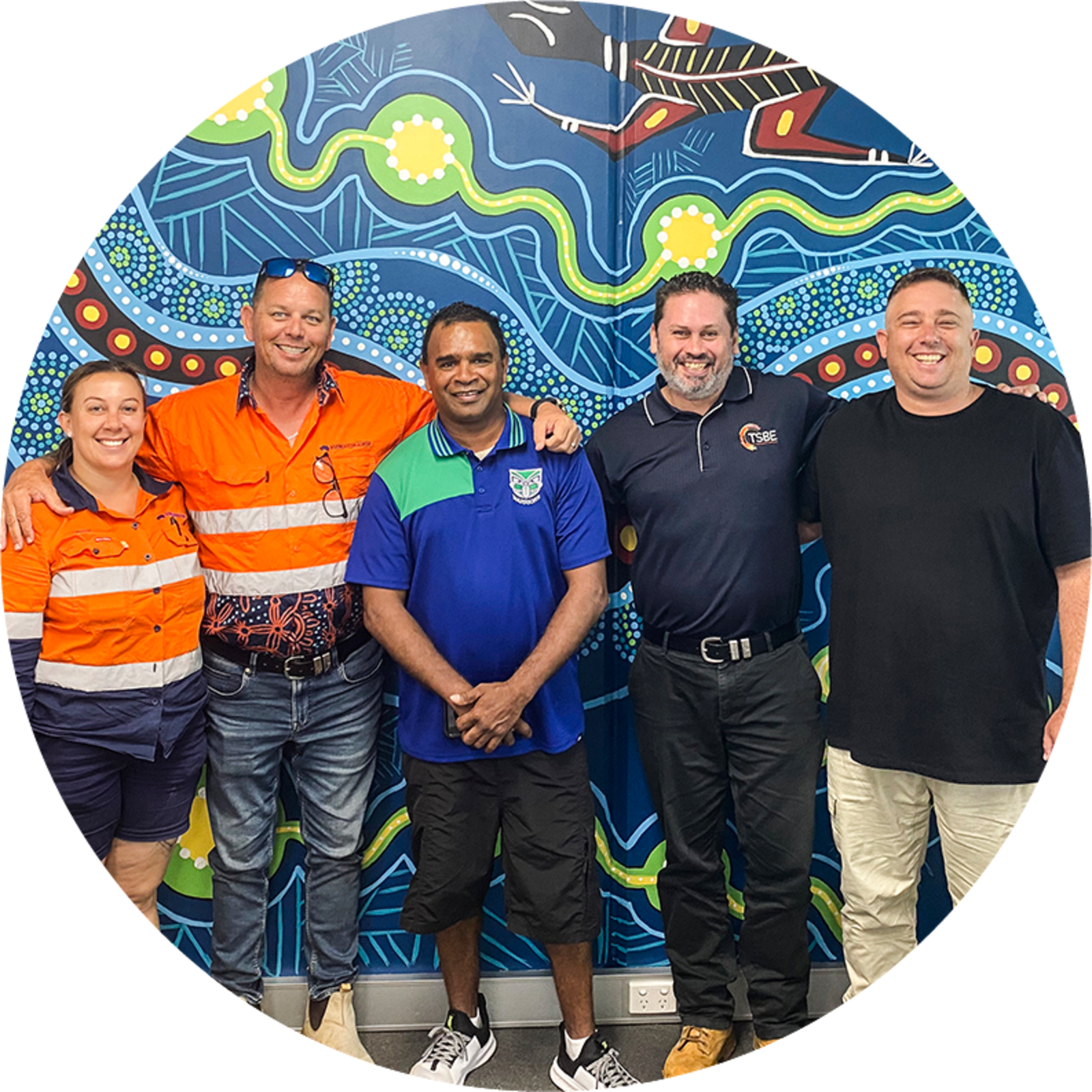People in polo shirts smiling in front of First Nation artwork