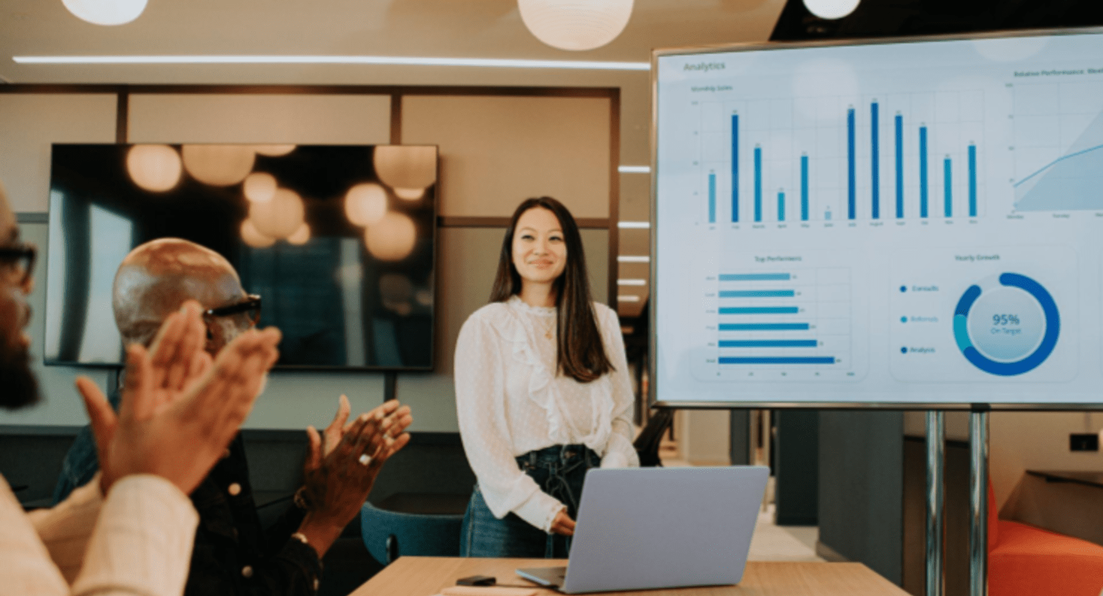 Businesswoman being applauded standing in front of a slide showing various graphs