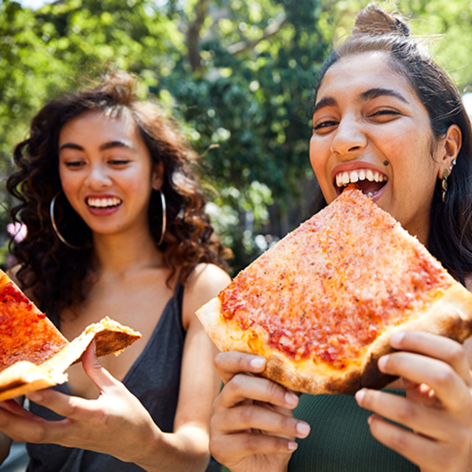 Two women smiling, eating large slices of pizza