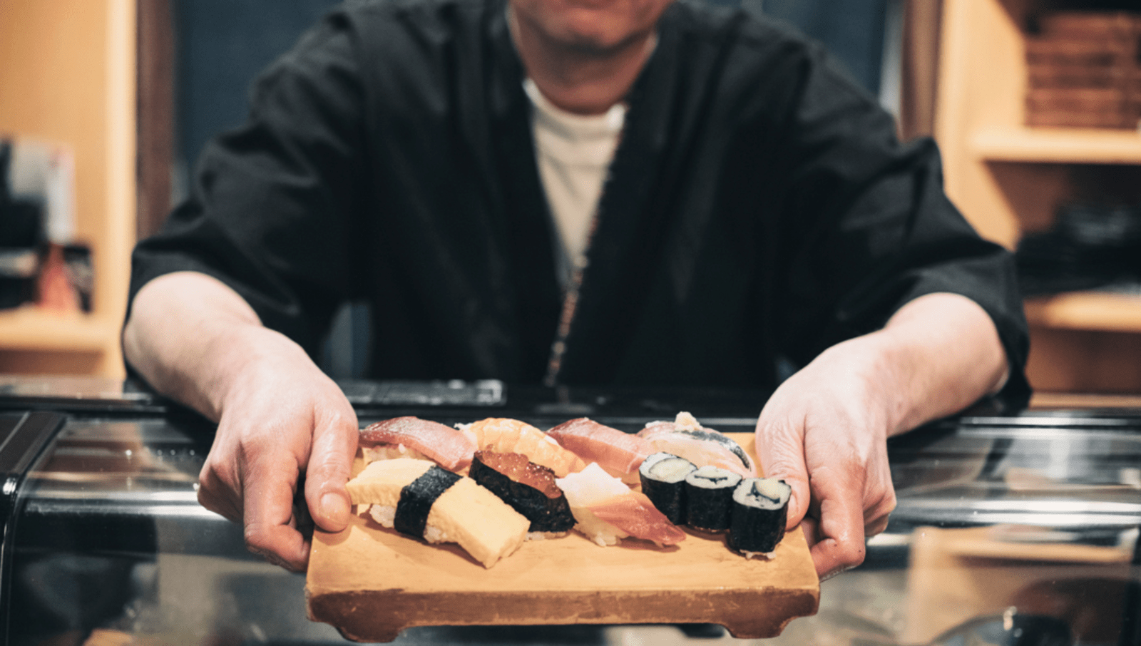 masc presenting chef handing over sushi in Tokyo 