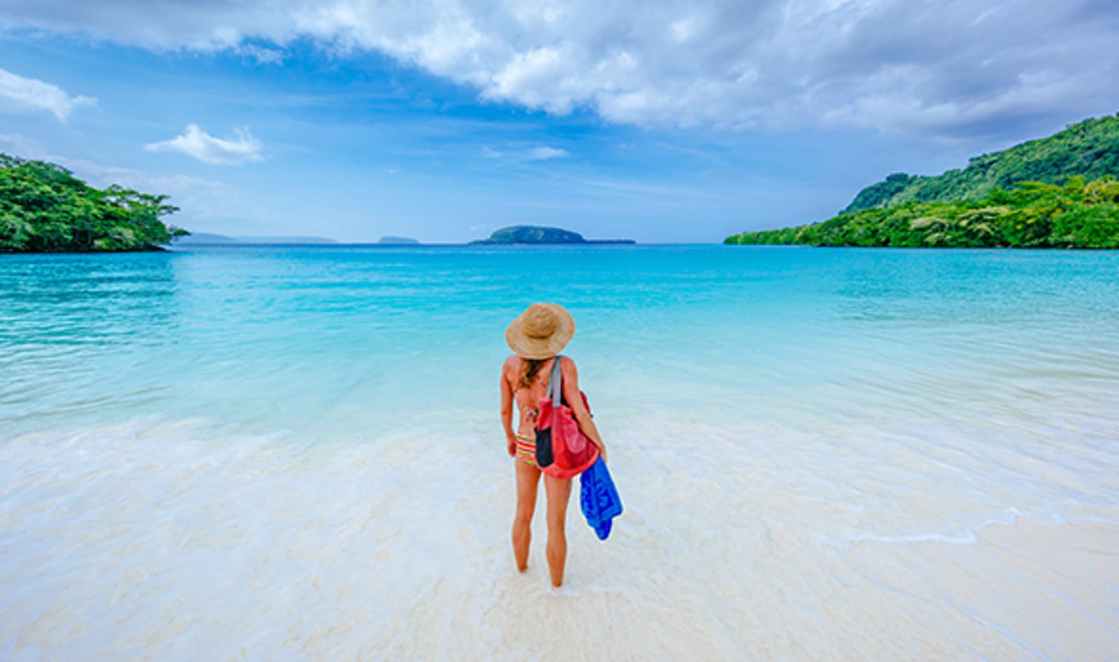 Women standing in shallow ocean water, looking out at tropical islands