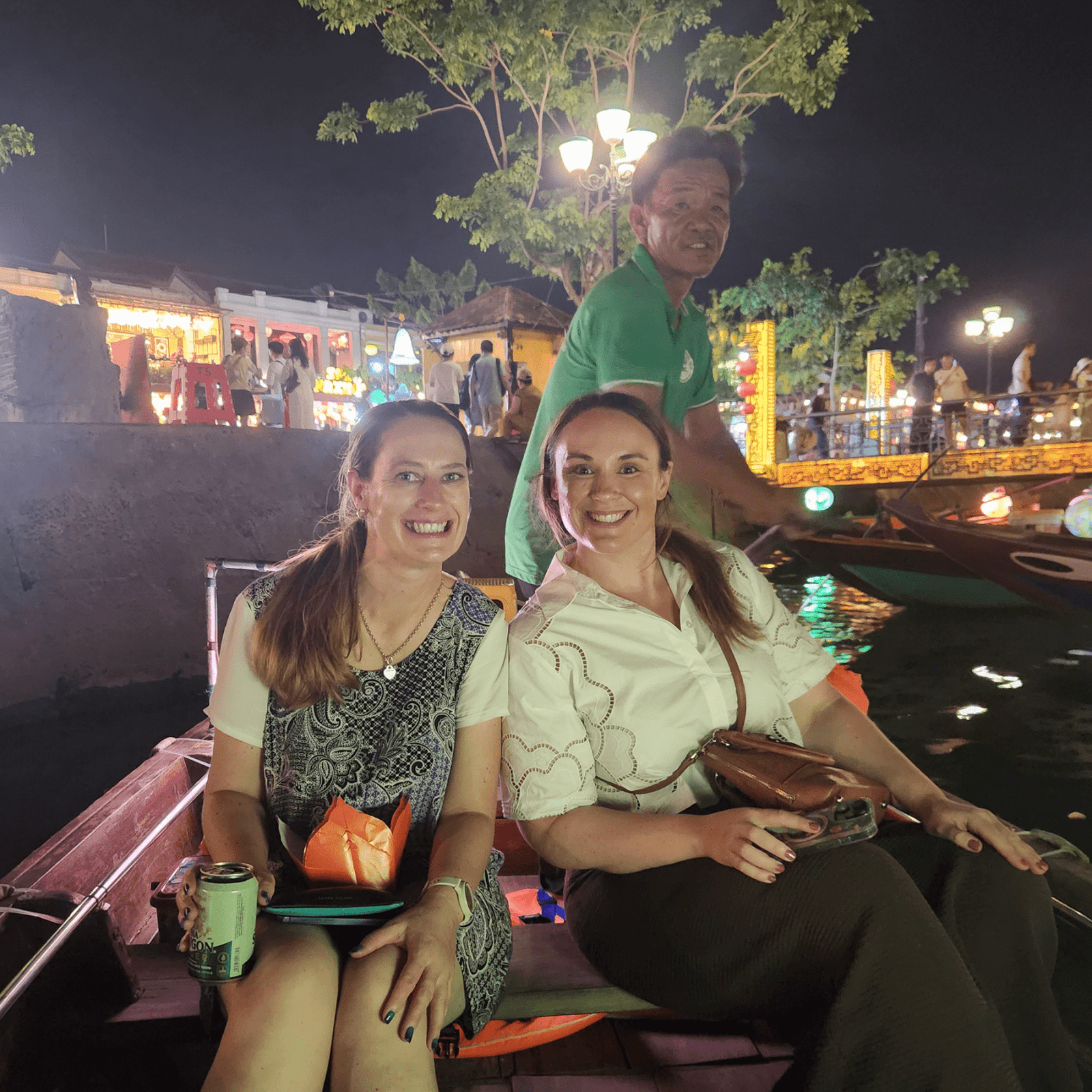 Two woman on a rowboat, sailing past brightly-lit markets in Hoi An, Vietnam