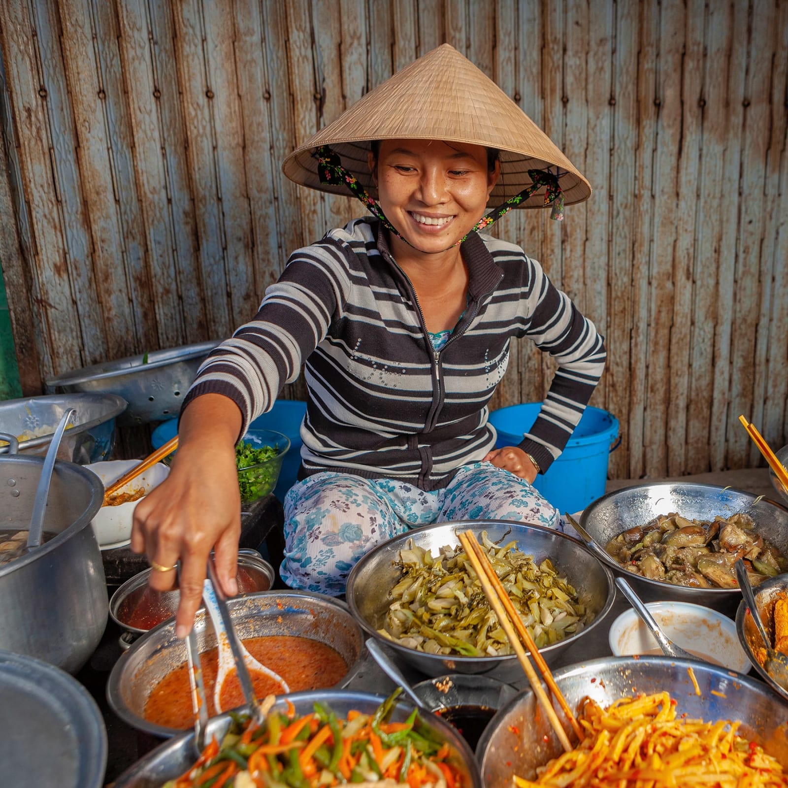 Woman in Vietnam smiling, serving food from several metal bowls