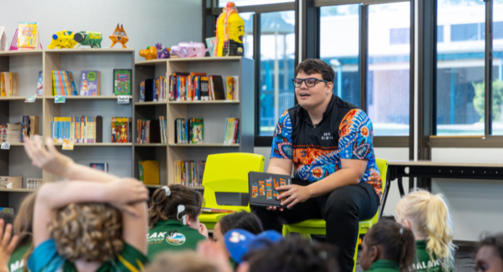 Man wearing a first nations-patterned shirt talking to school children in a library