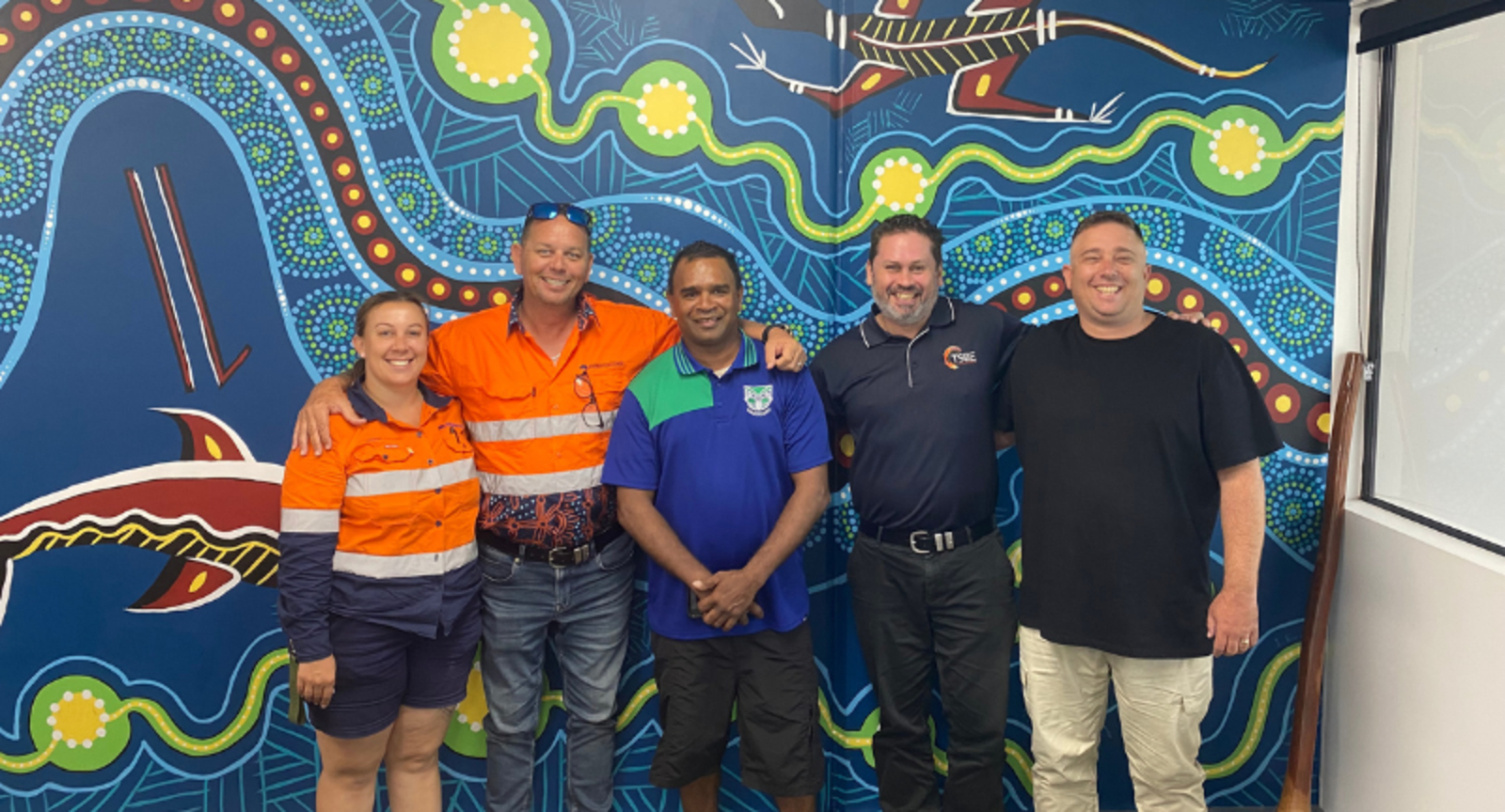 Tradespeople and businessmen standing in front of Australian First Nations artwork
