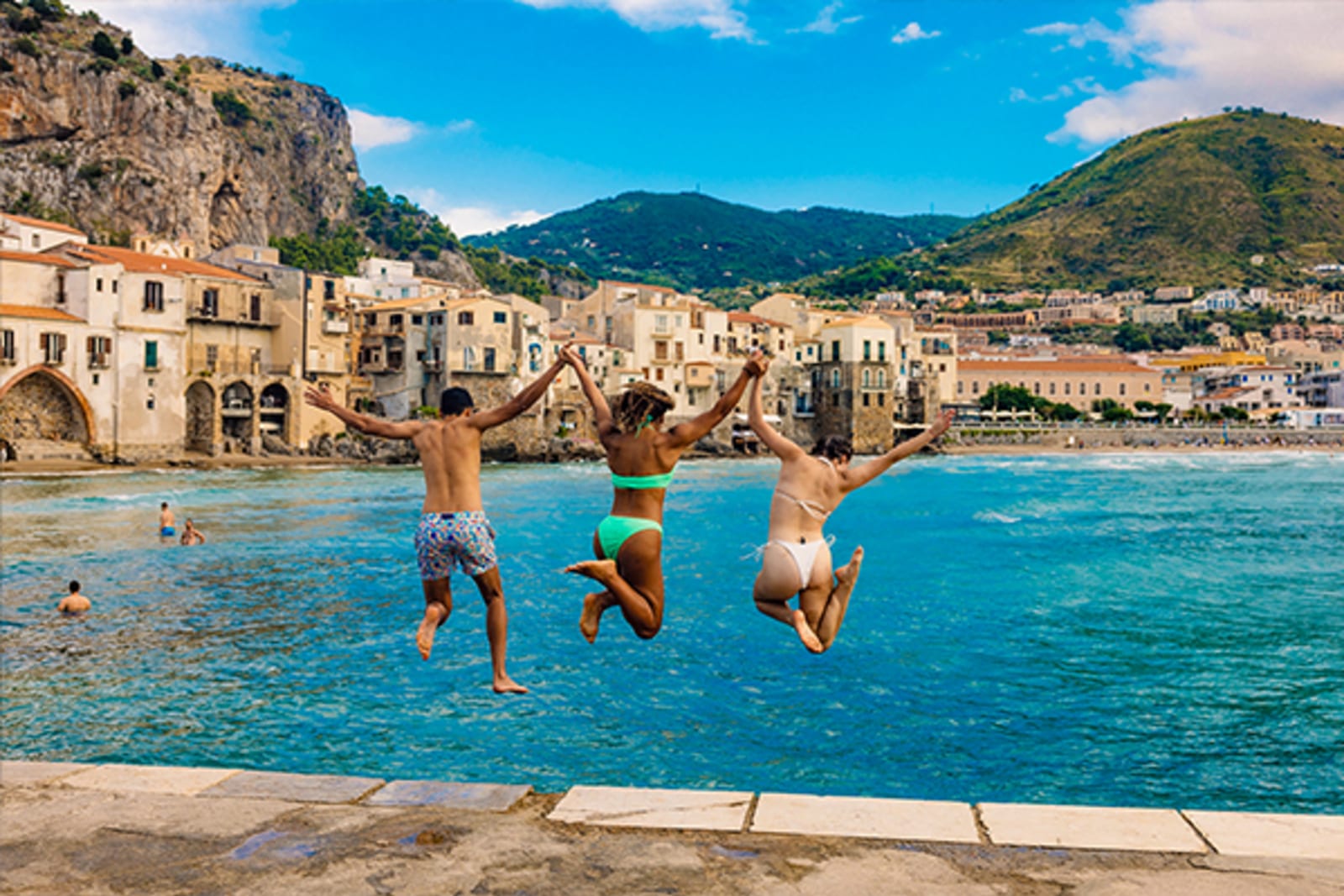 Three people jumping into the ocean from a pier in Europe