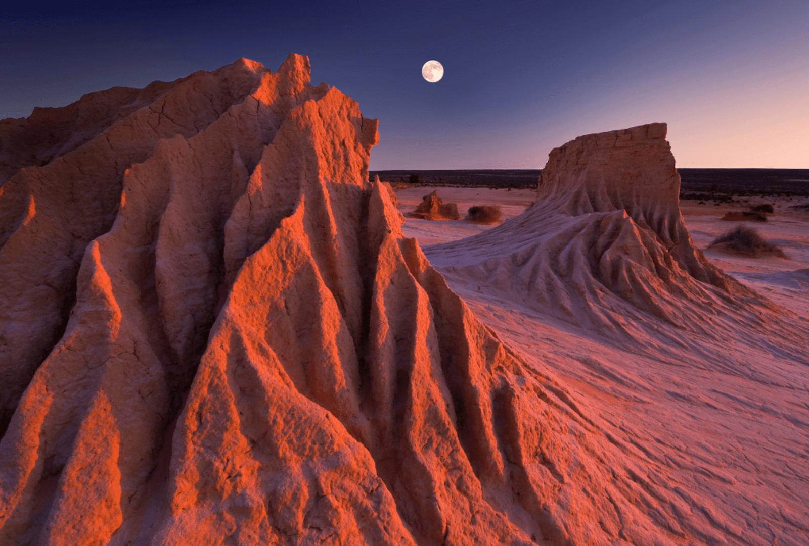 The full moon rises while the sun sets simultaneously at the ancient sandstone rock formations known as the Walls of China at Mungo National Park