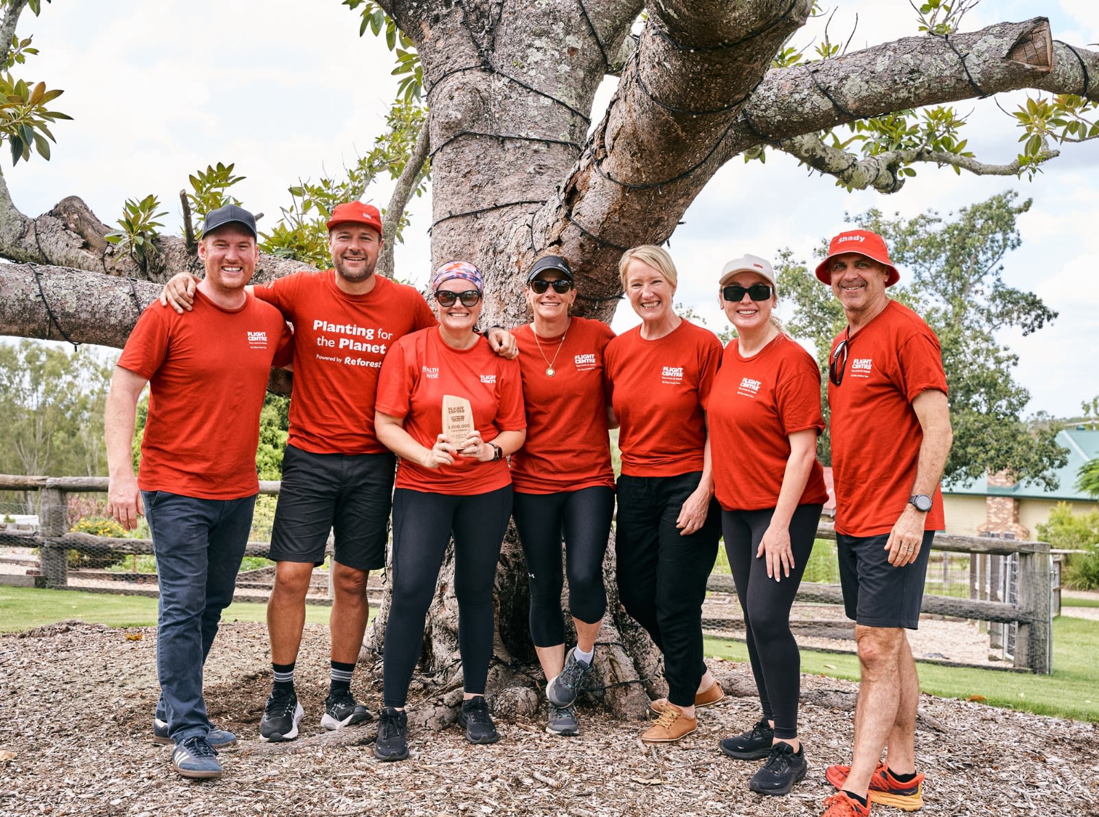 group of flight centre employees in red shirts standing by tree