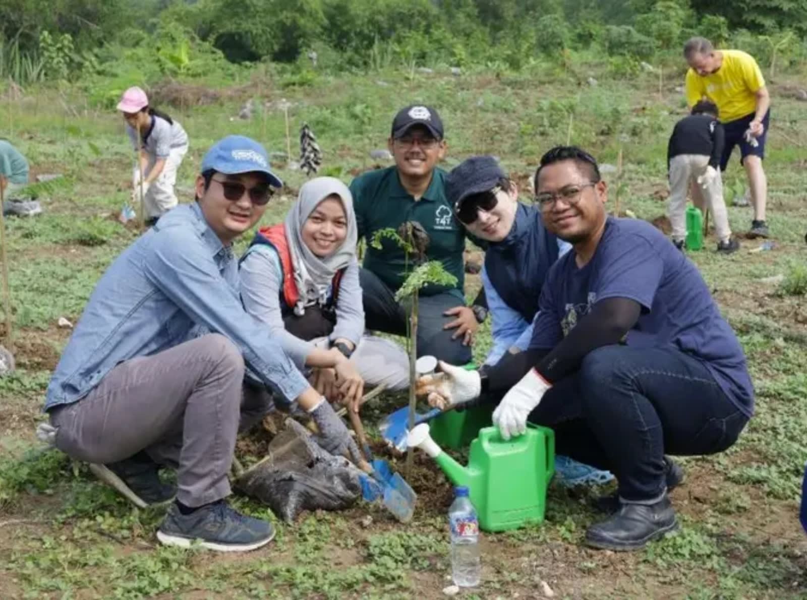 five people standing around tree being planted