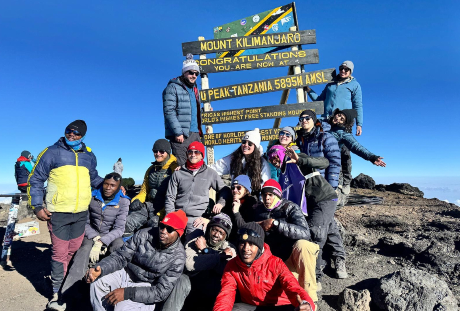 A group of hikers pose for a photo atop the rocky summit of Mount Kilimanjaro