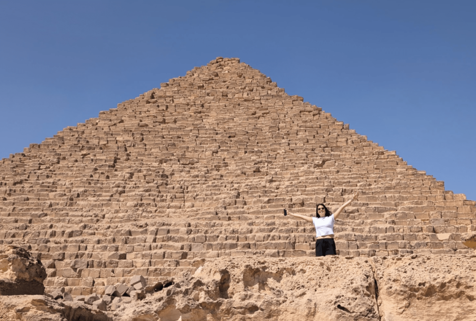 A woman waves while standing at the base of one of the Pyramids of Giza