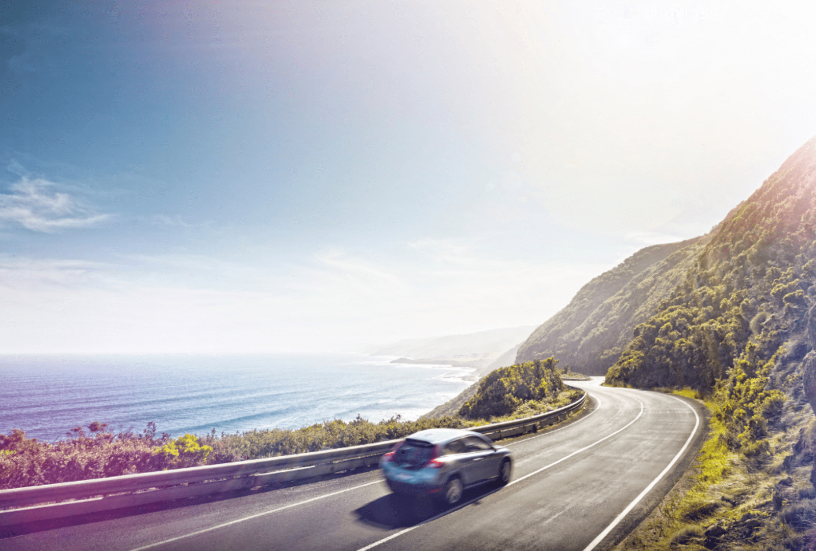 Cars drive along the Great Ocean Road on a sunny afternoon