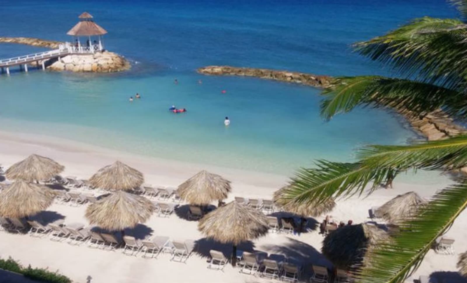 Overhead view of a beautiful cove with tourists relaxing, alongside a beach with deckchairs and grass-umbrella