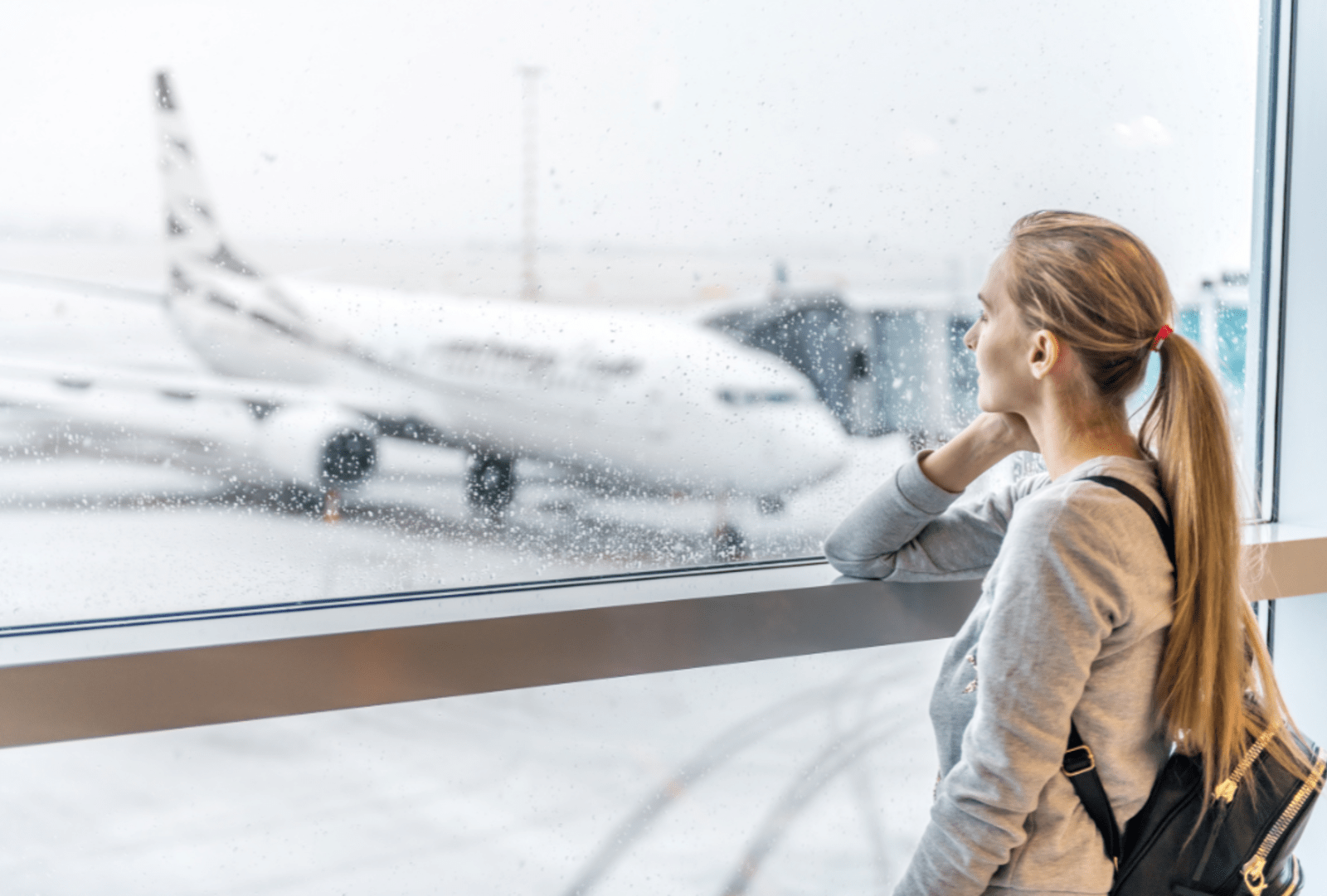  A woman with a light bag watches a plane from an airport window