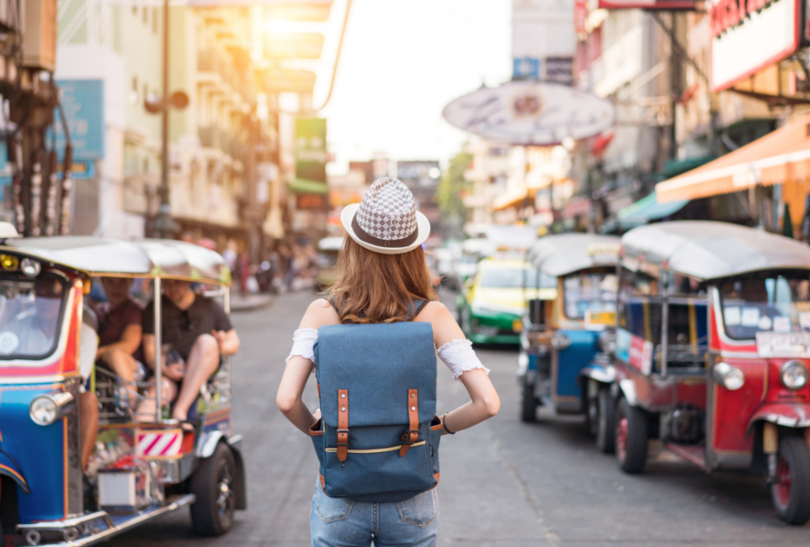 A woman stands on a street among tuk tuks