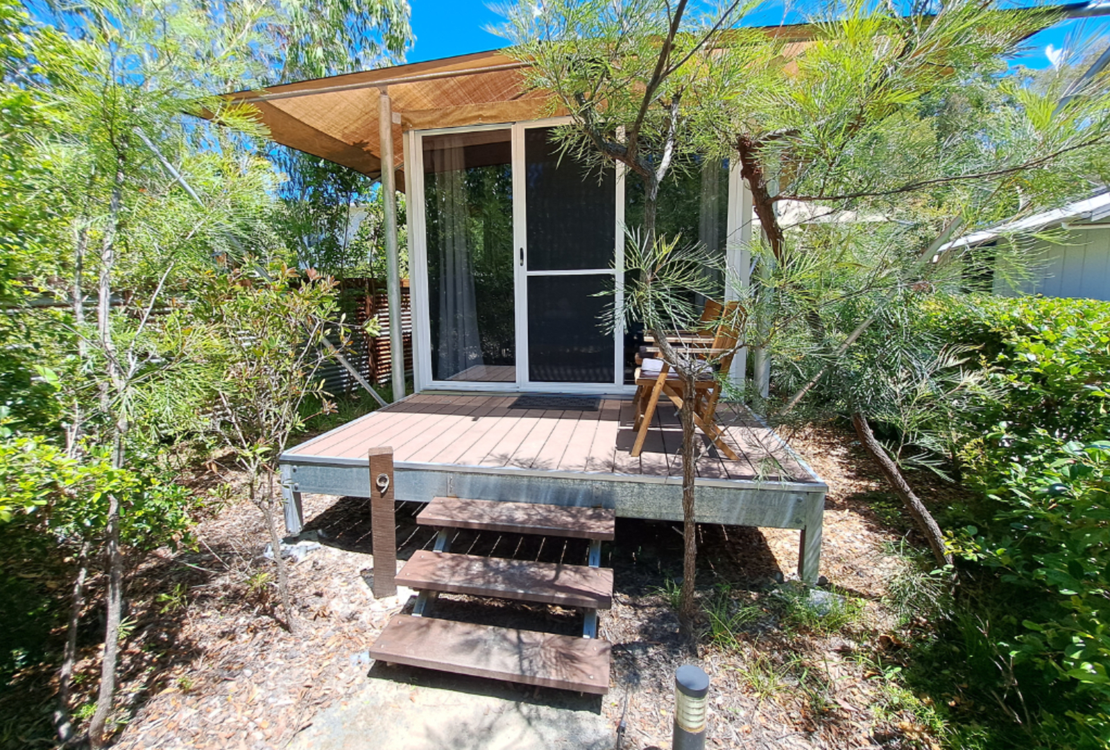 A 2-person glamping cabin set among shrubs under a blue sky.
