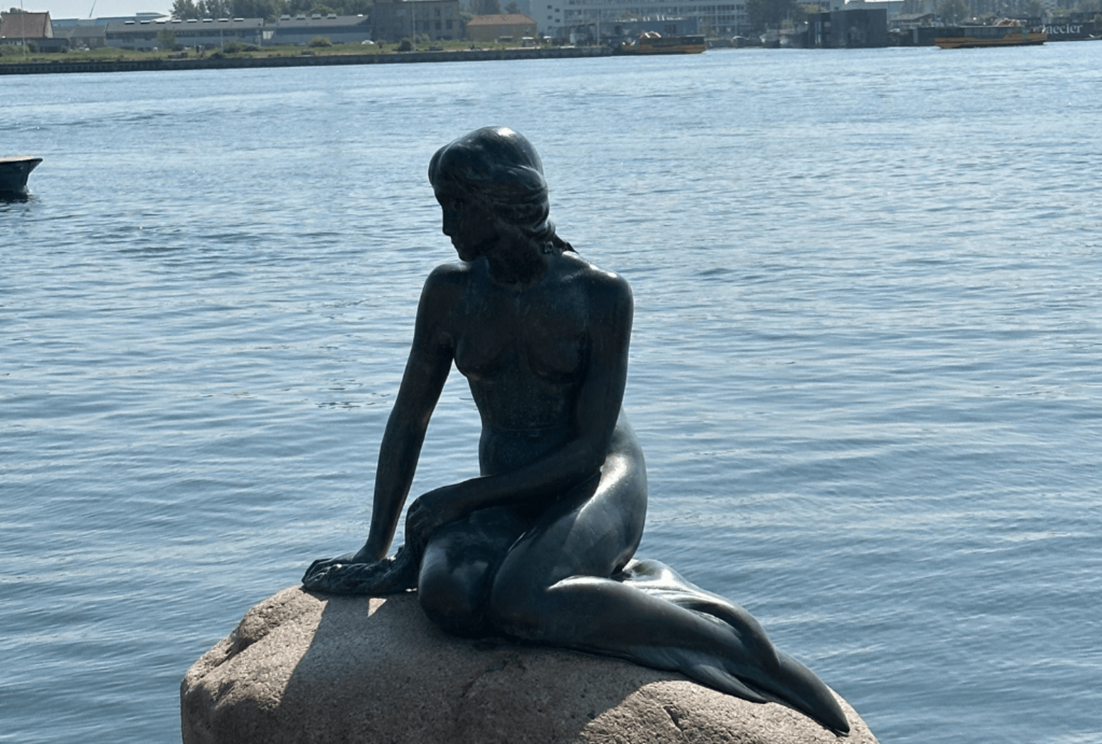 A bronze statue of Hans Christian Andersen's Little Mermaid sits on a rock by the sea at Copenhagen