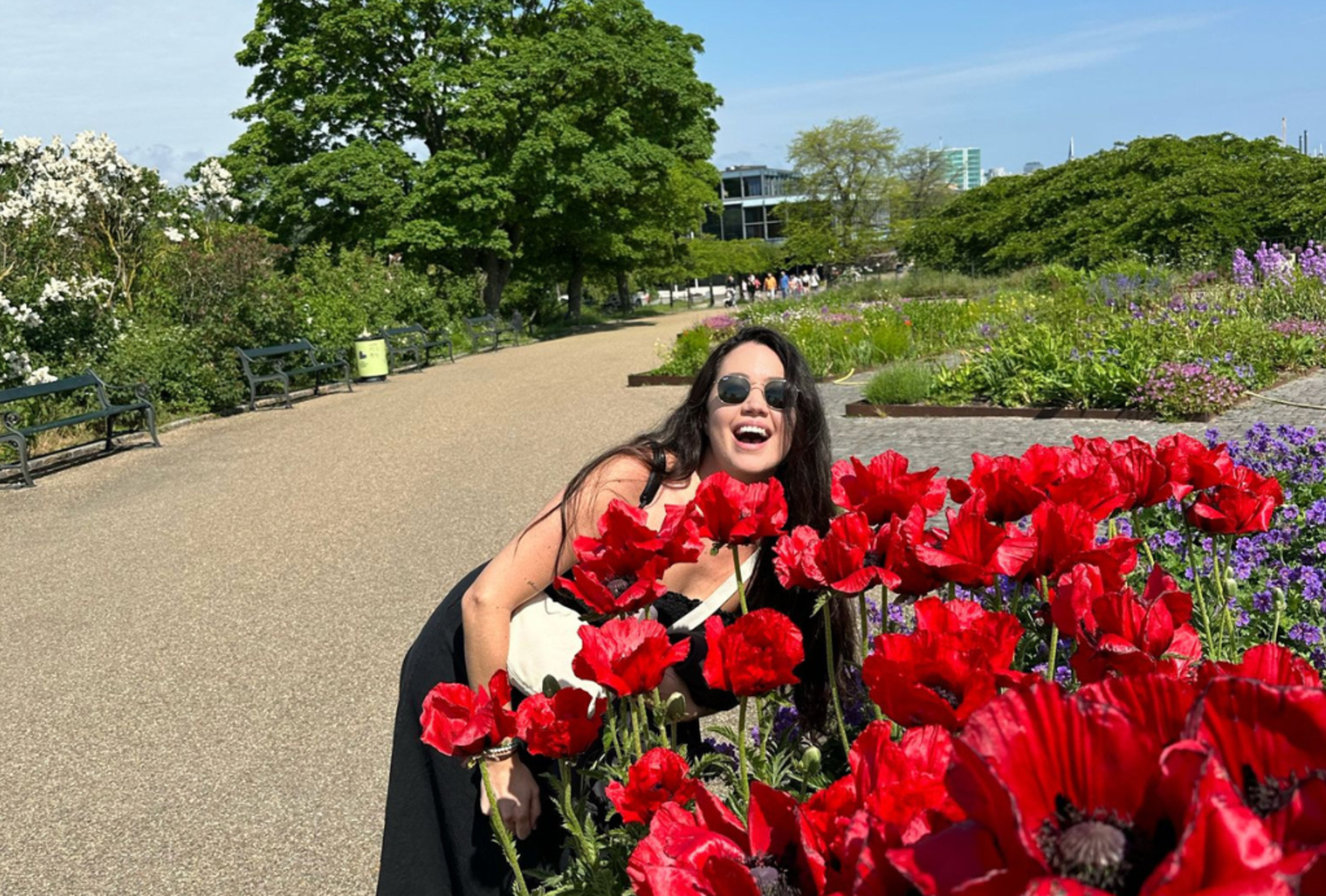 Sara smiles by a bloom a of big red flowers at the Rosenborg Gardens in Copenhagen