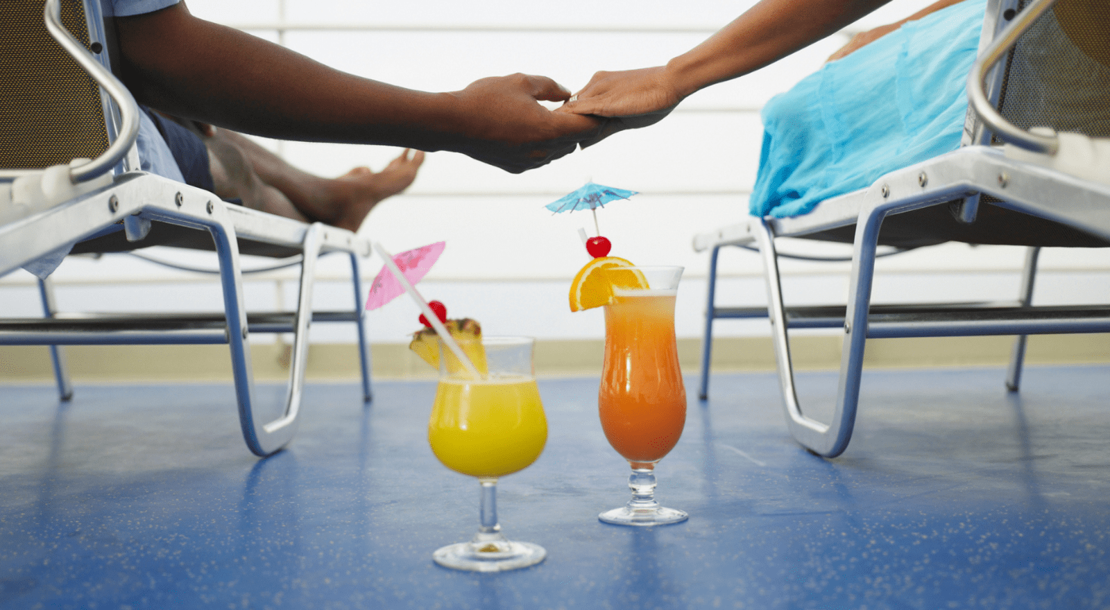 A couple lie in deck chairs holdings hands with cocktails