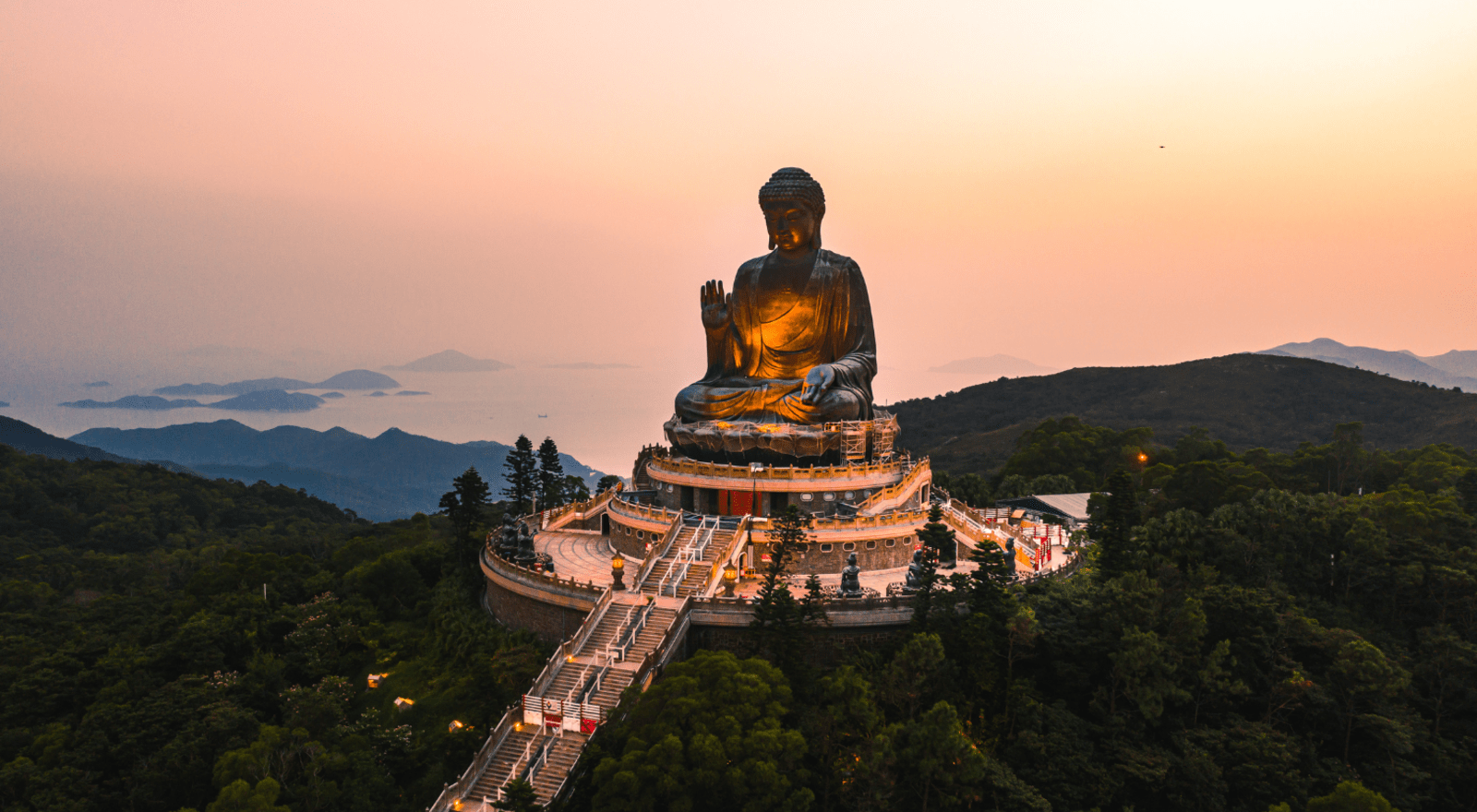 The giant bronze Buddha at Po Lin Monastery towers over hills and islands at sunset