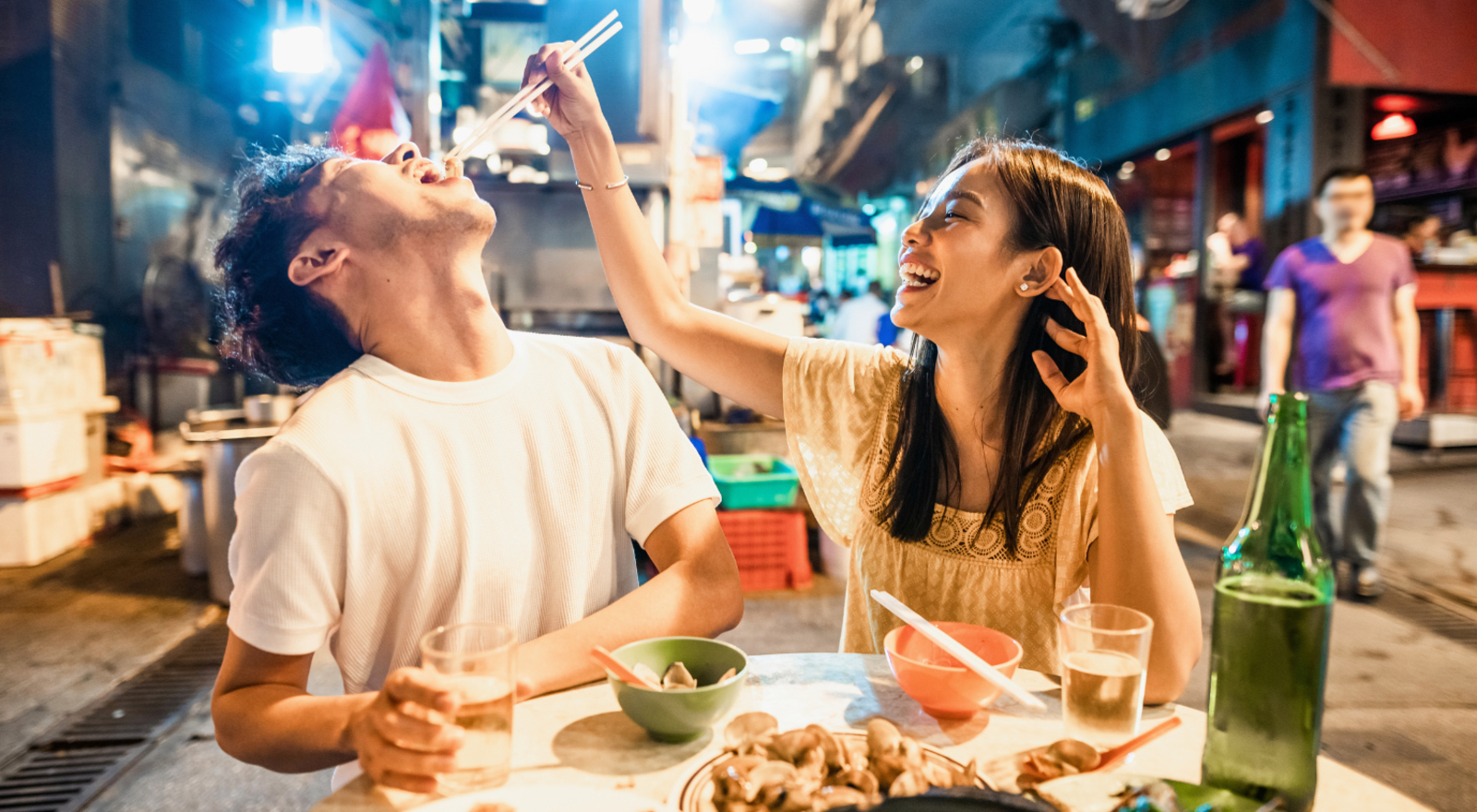 A woman holding chopsticks drops food in the mouth of a man which can best be described as culinary eroticism