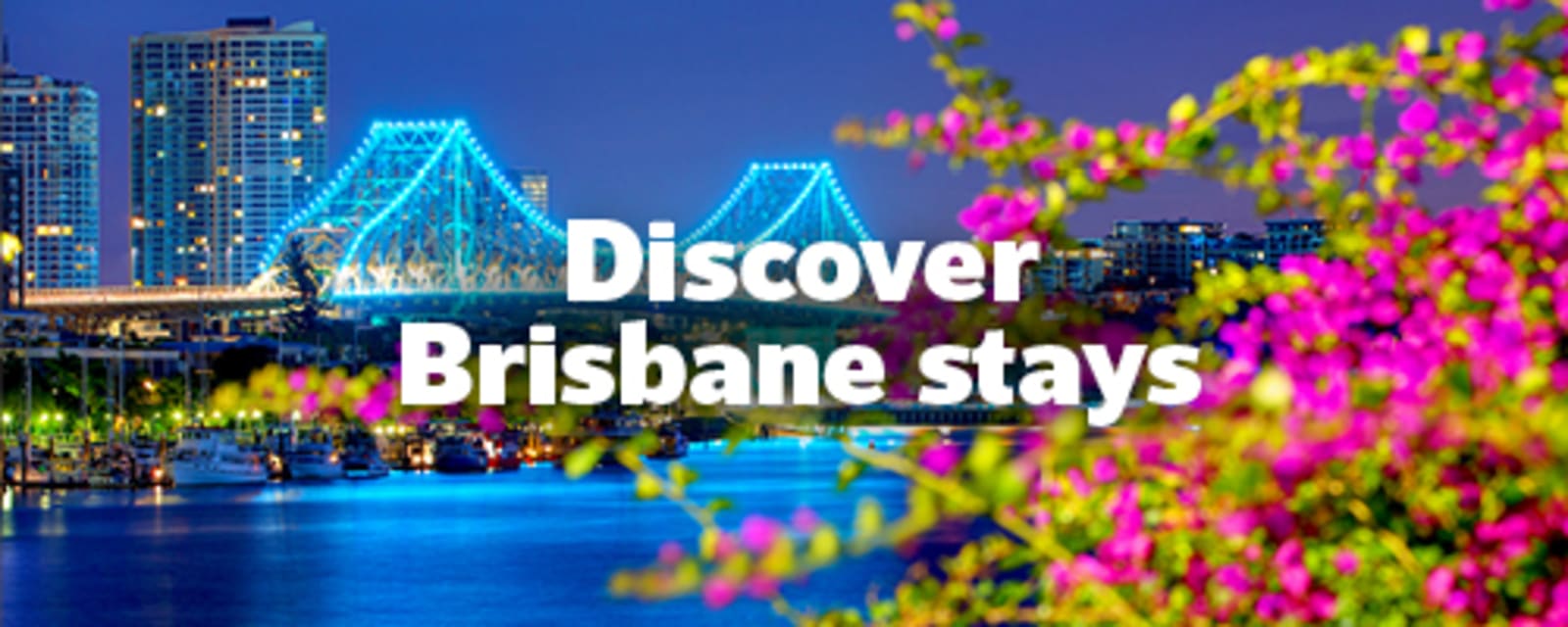 Story Bridge lit up over the river beside Brisbane skyline and blossoms for Discover Brisbane stays