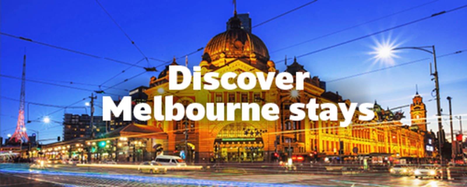 Flinders Street Station glowing at night with light trails through Melbourne city for Discover Melbourne stays