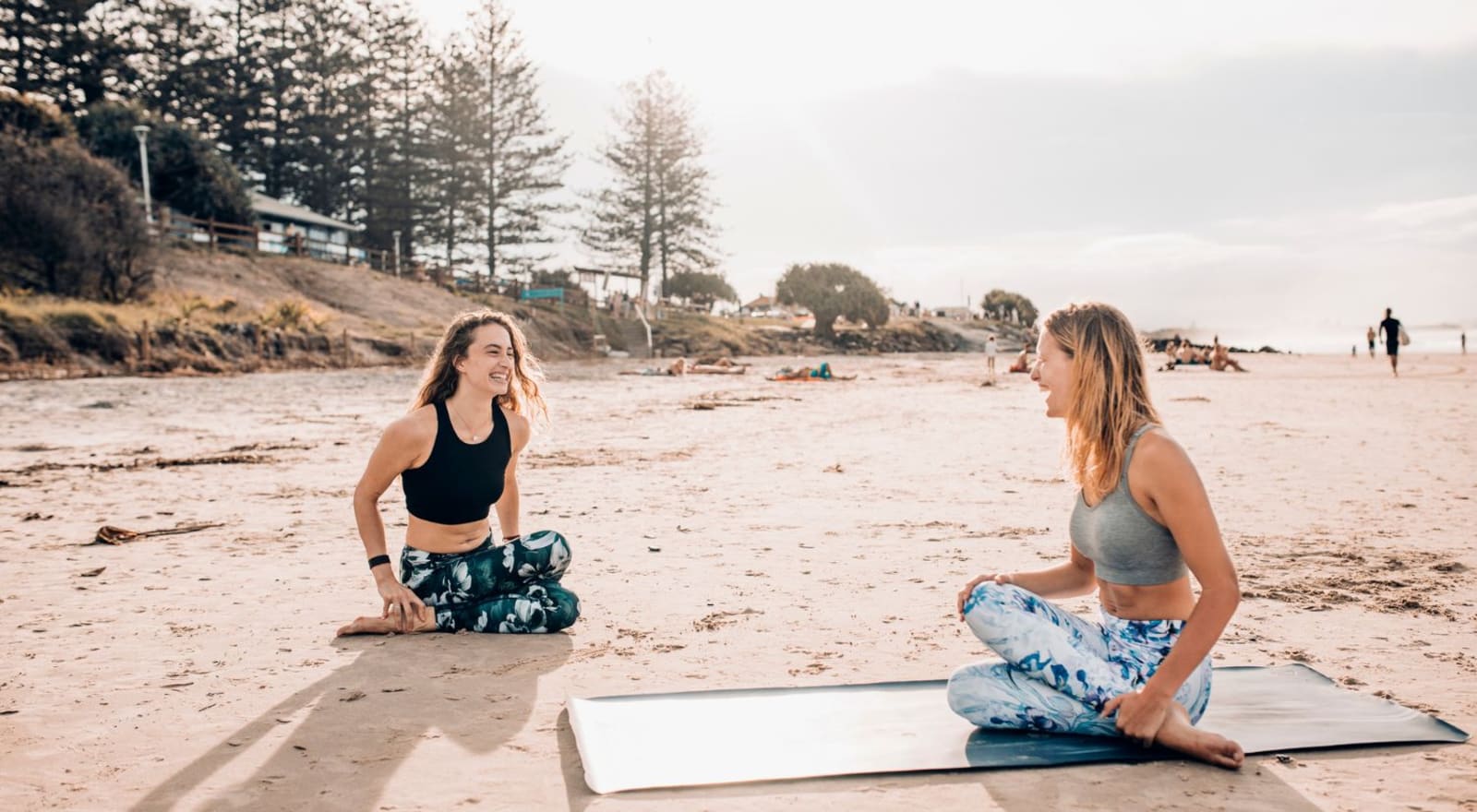 two women sitting in yoga poses on the beach