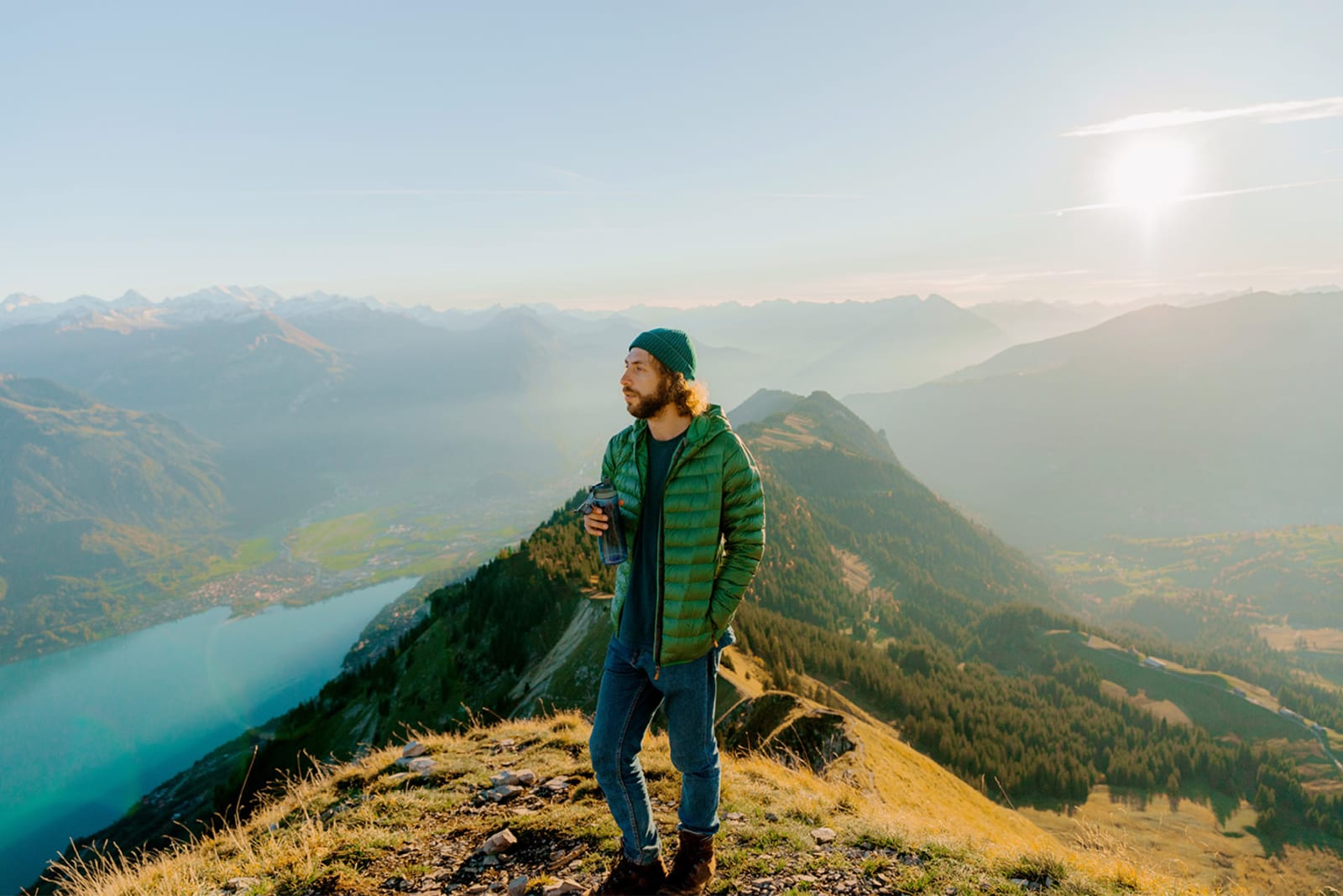 A hiker standing at the top of a mountain peak with a re-usable water bottle in their hand