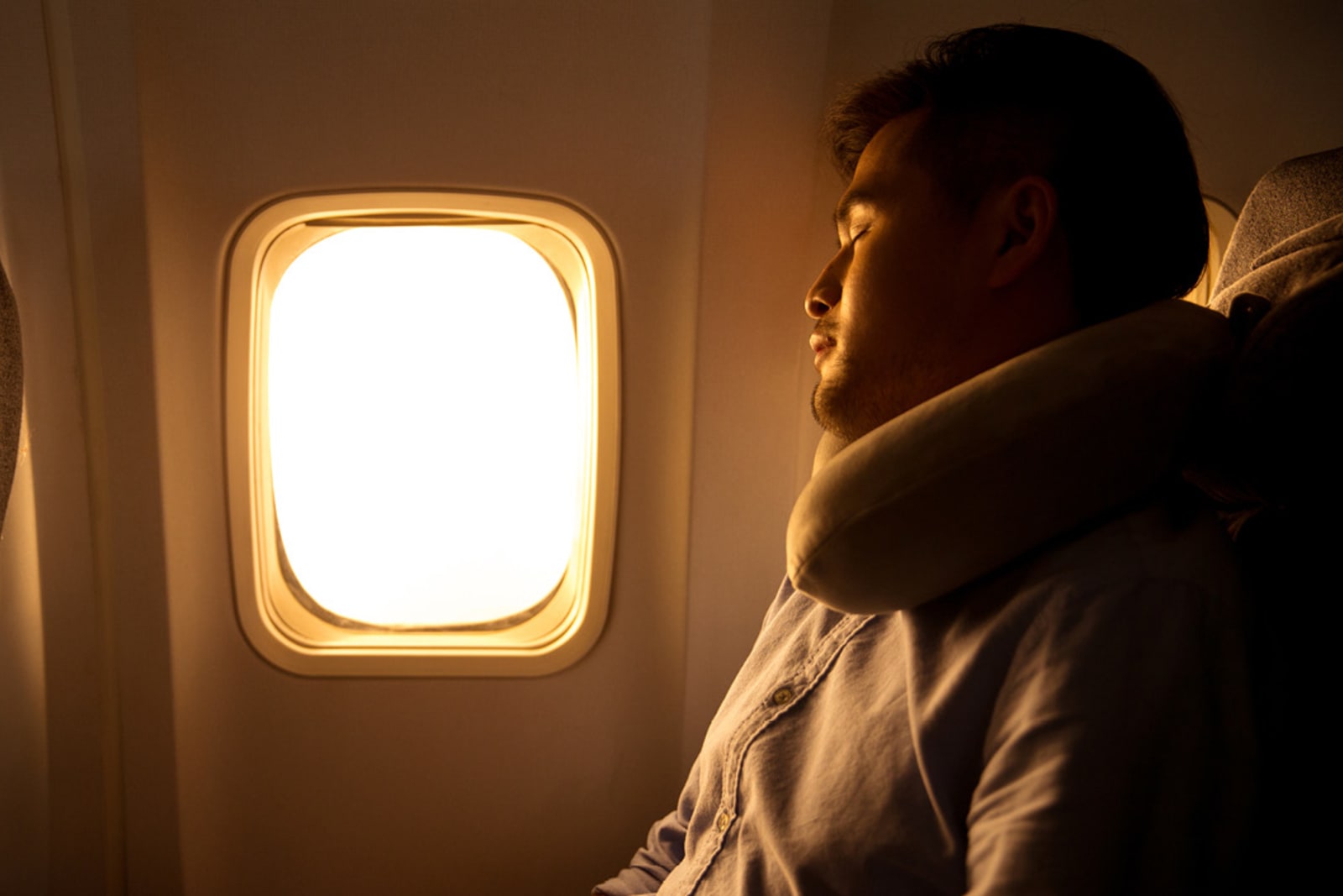 A man wearing a neck pillow sleeping on a plane