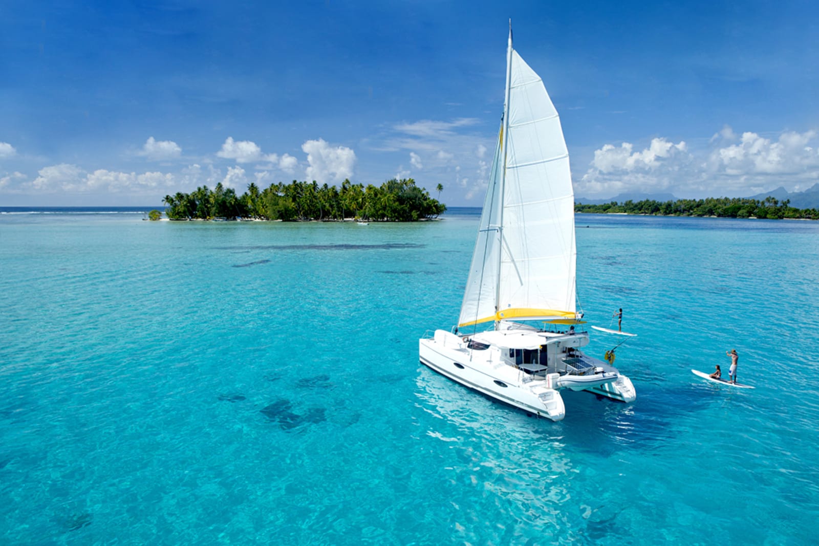 A catamaran with people paddleboarding around the islets of Tetiaroa