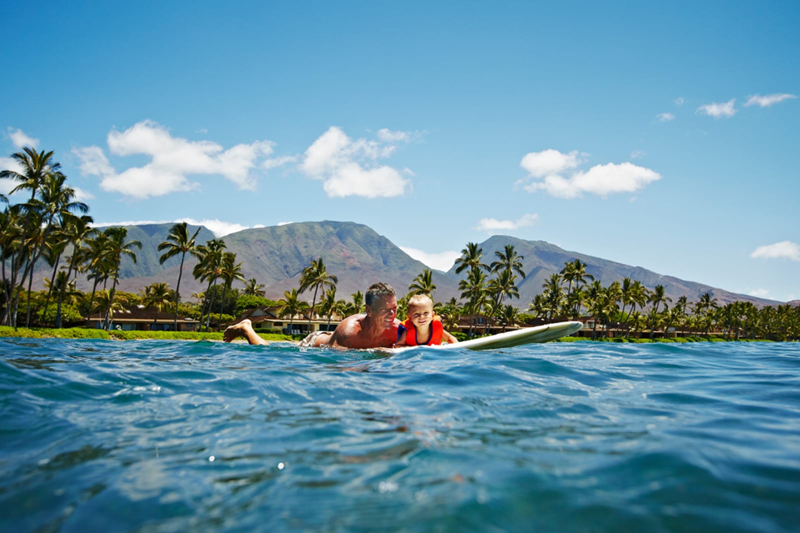 A father and his young son floating on a surfboard in Hawai‘i