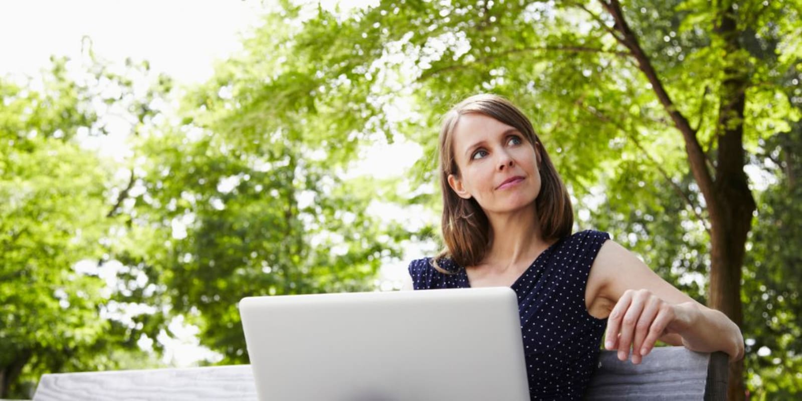 A business woman on a laptop sitting in a park with trees in the background