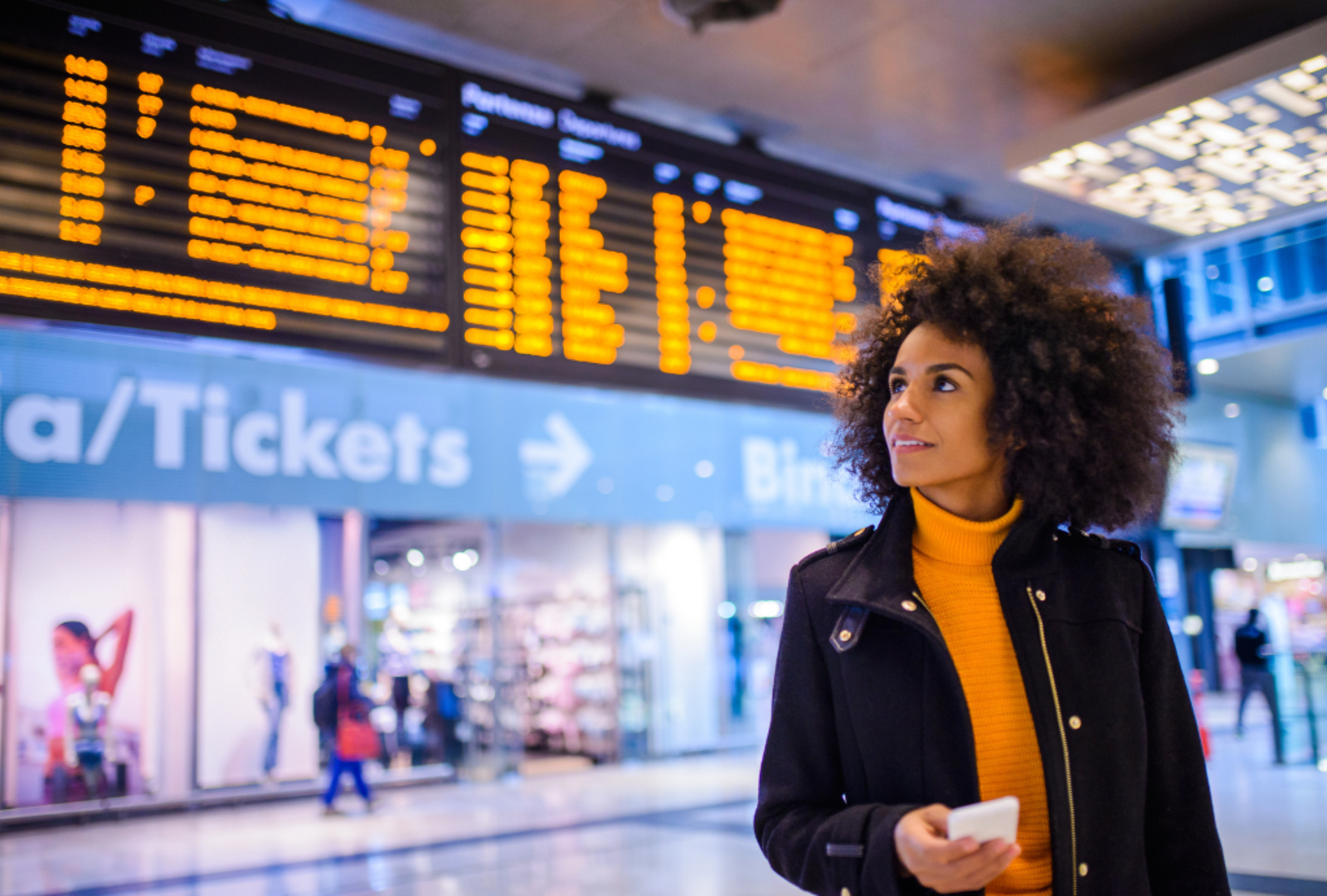 A woman at an airport checks flight times on an overhead digital display