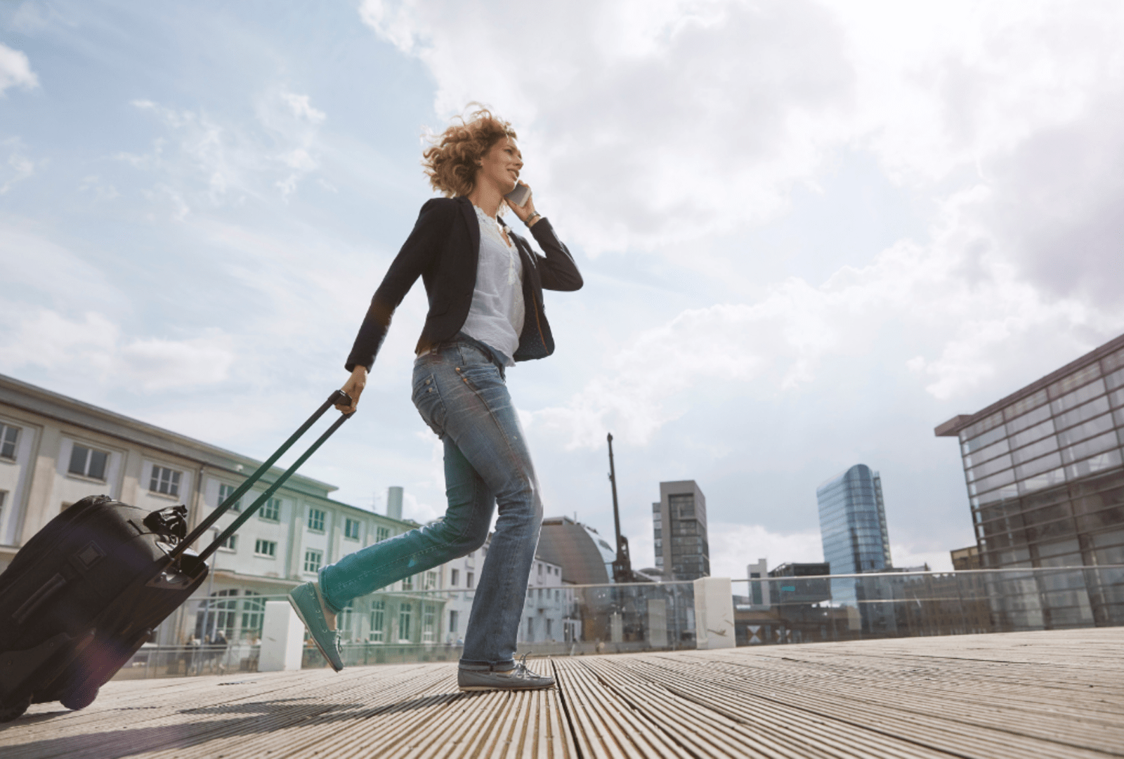 Woman on the phone walking with a rolling suitcase in the city