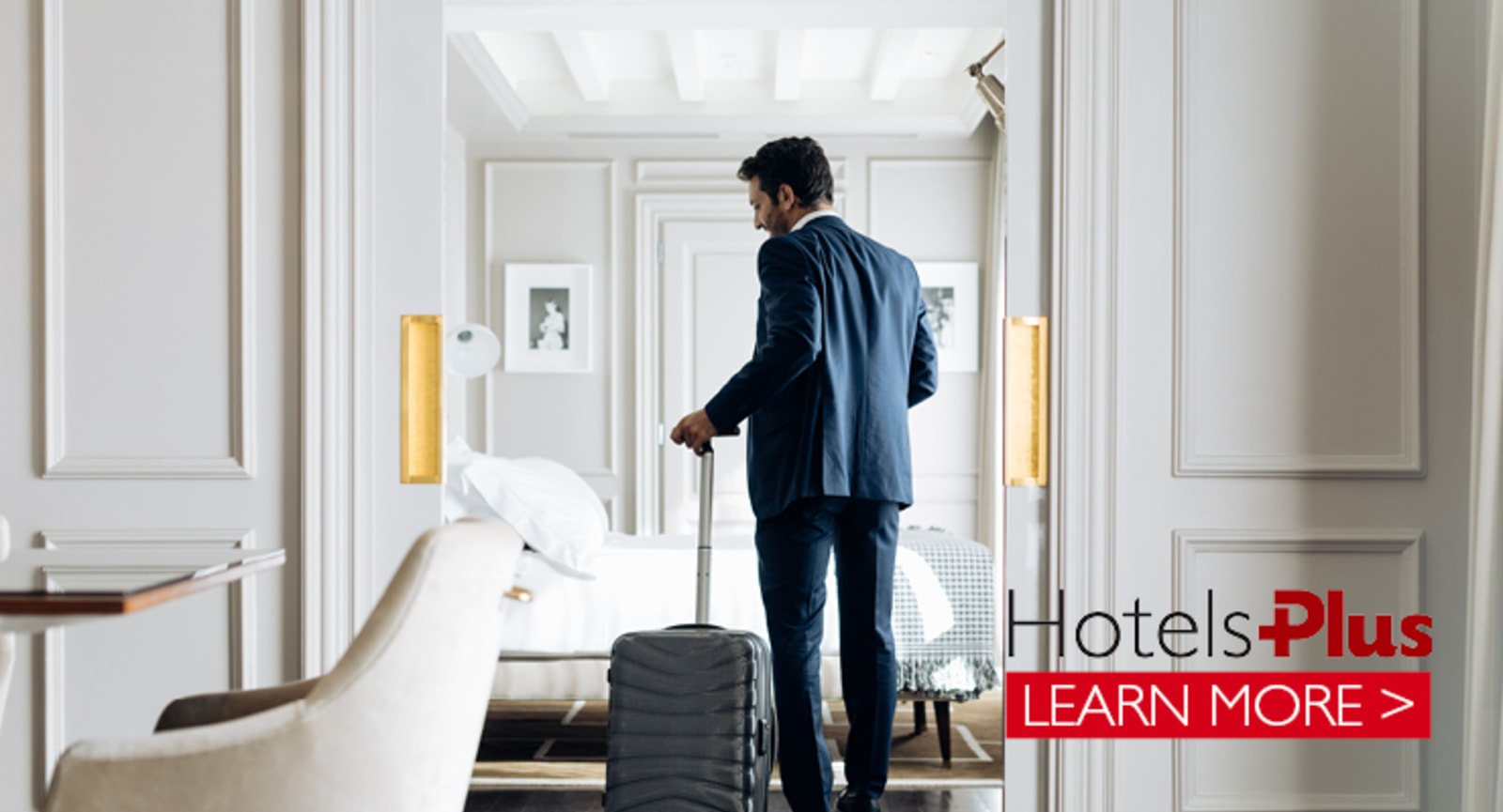 Back of a businessman with rolling luggage standing in a bright white hotel room