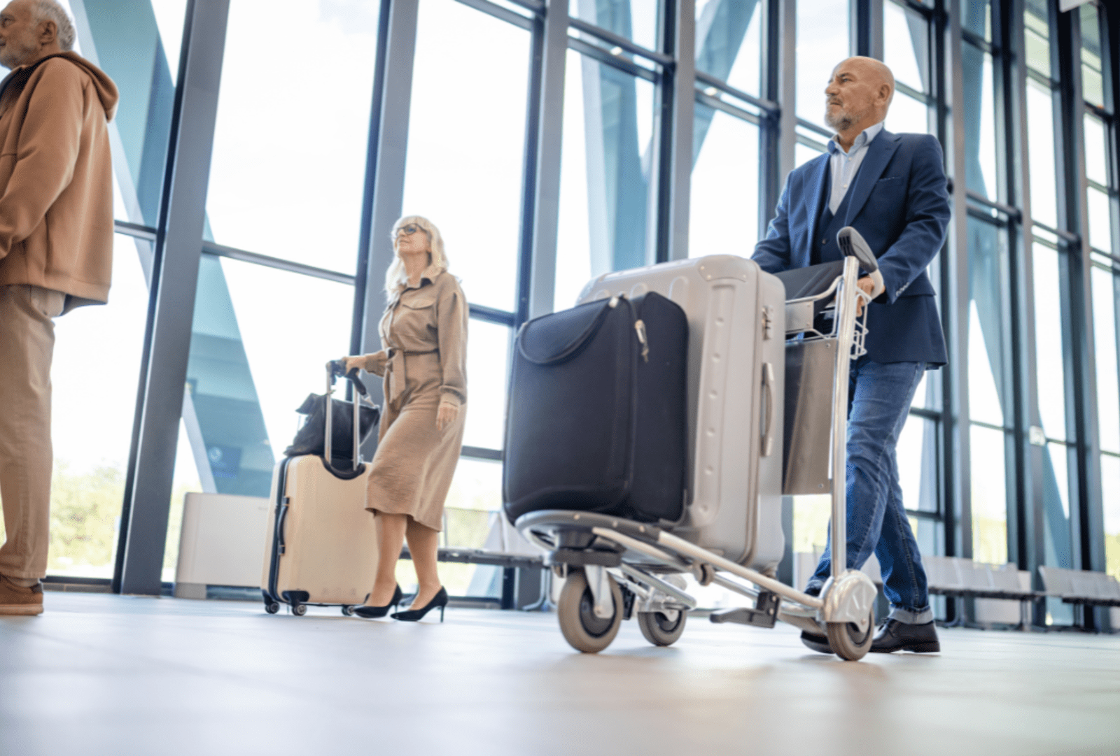 A man walks through an airport pushing a cart full of suitcases