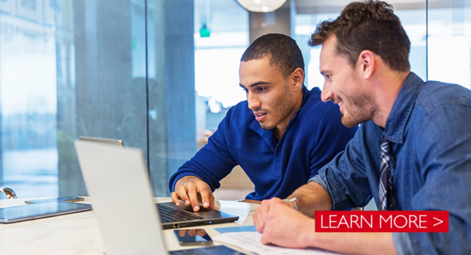 Two businessmen working on laptops in a glass room