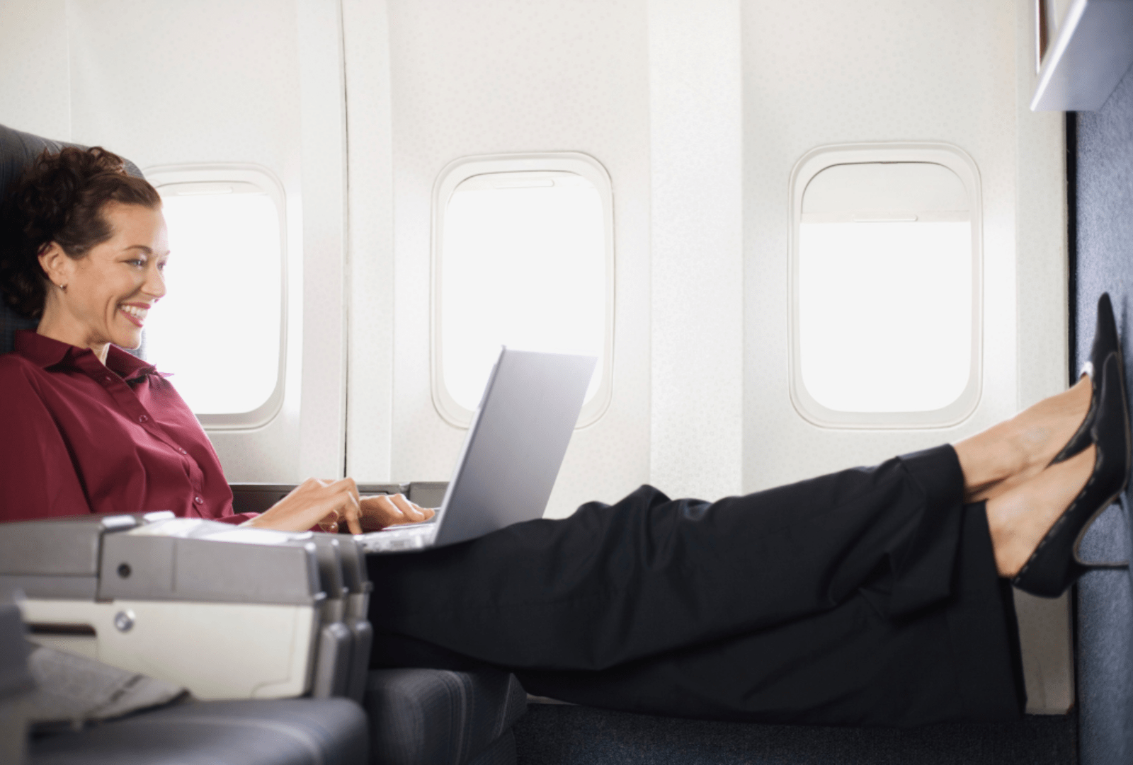 A business woman working on a laptop puts her feet up in business class