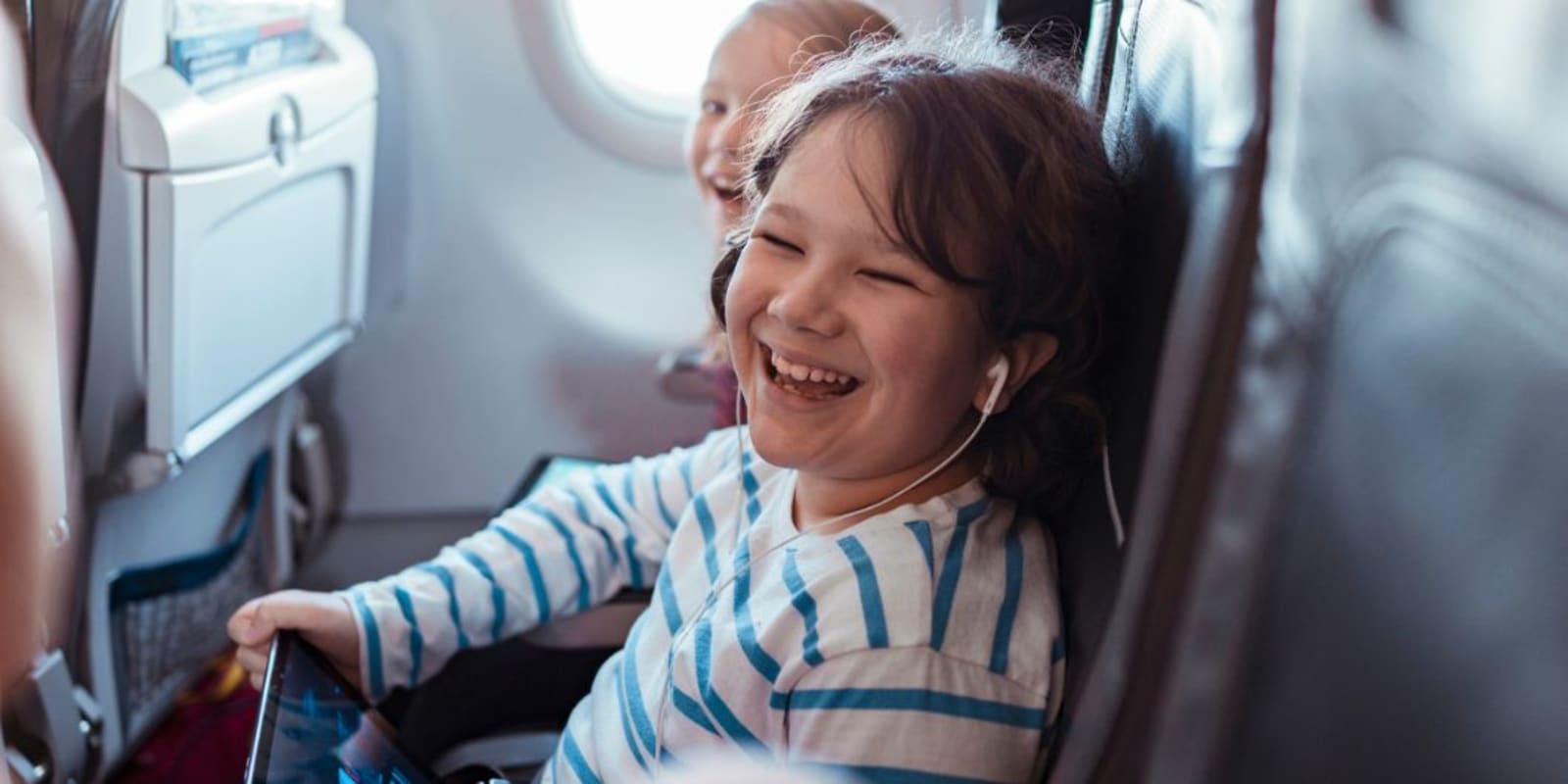 A young child on a plane with headphones in laughing