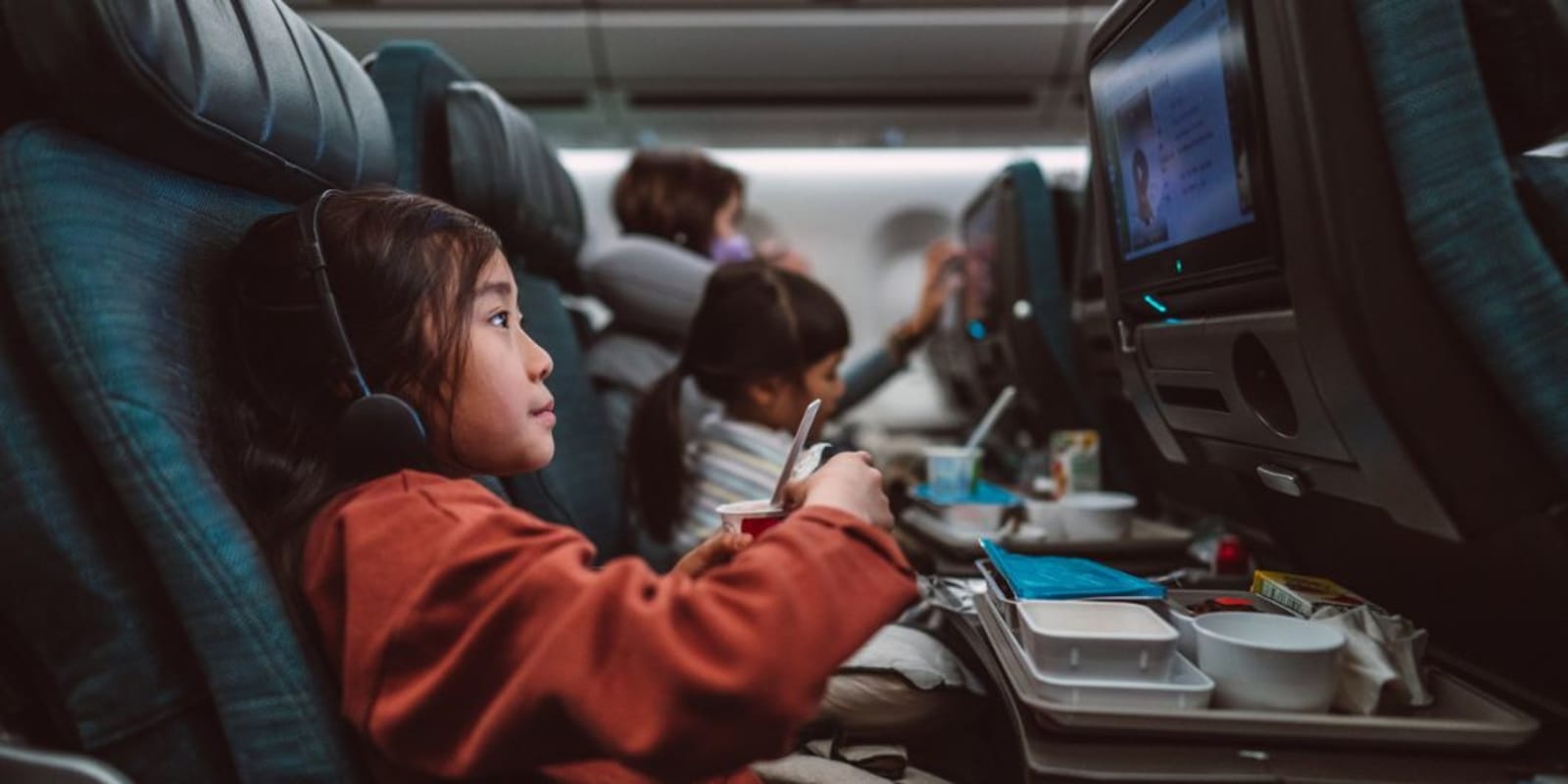 A young child on a plane with headphones on watching a tv screen