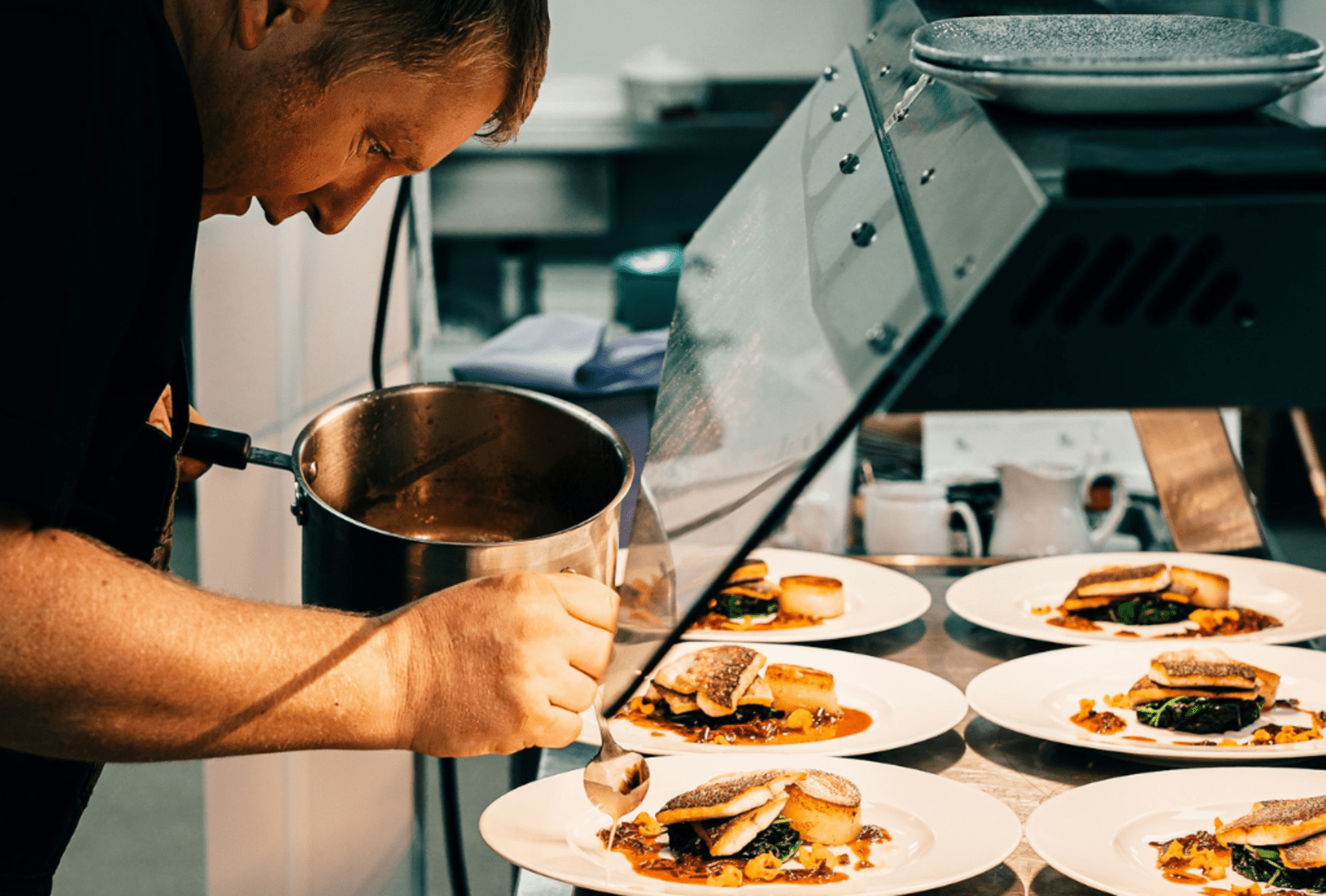 A chef plating meals on white plates from a pot