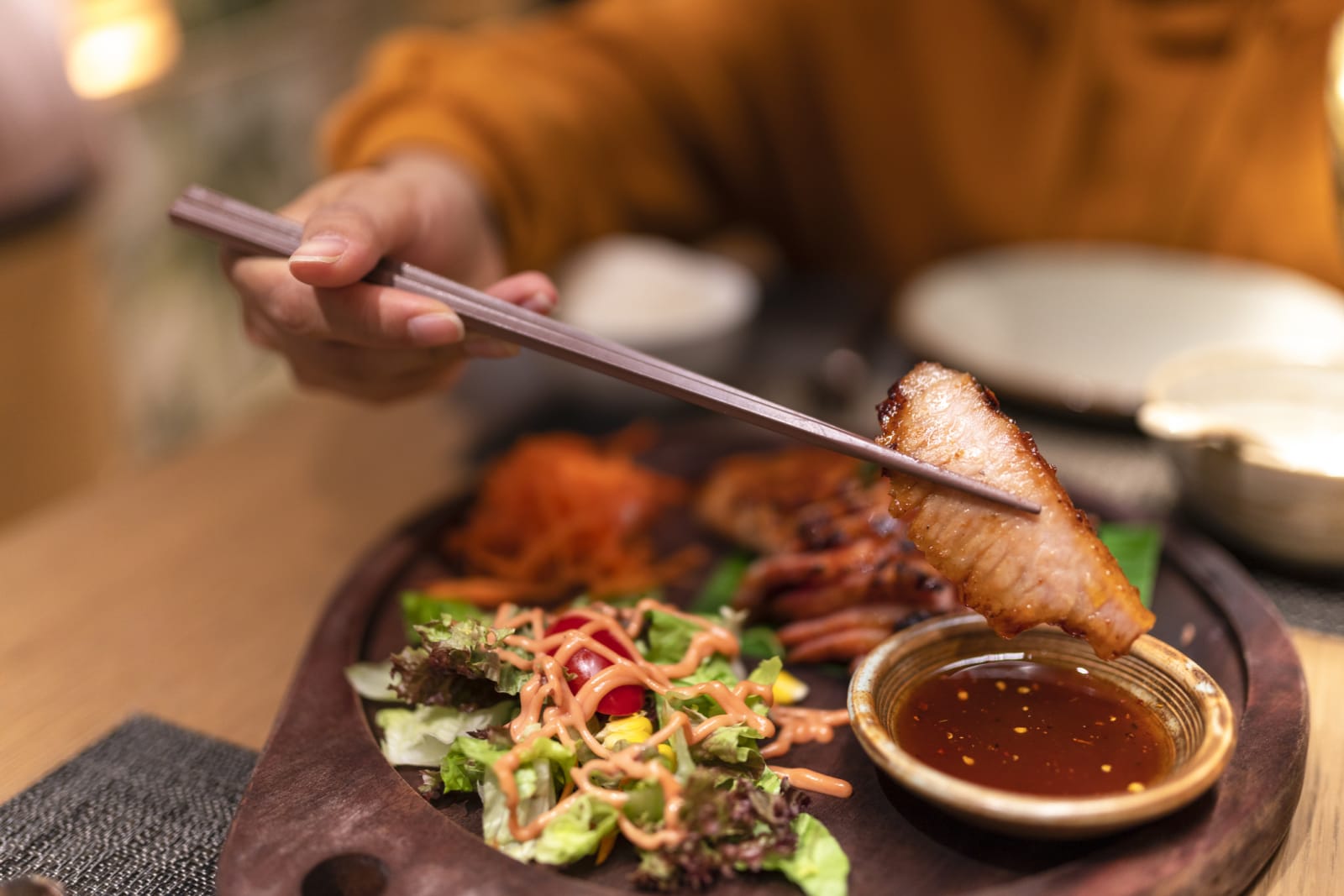 person eating thai food picking up meat with chopstick and dipping into sauce