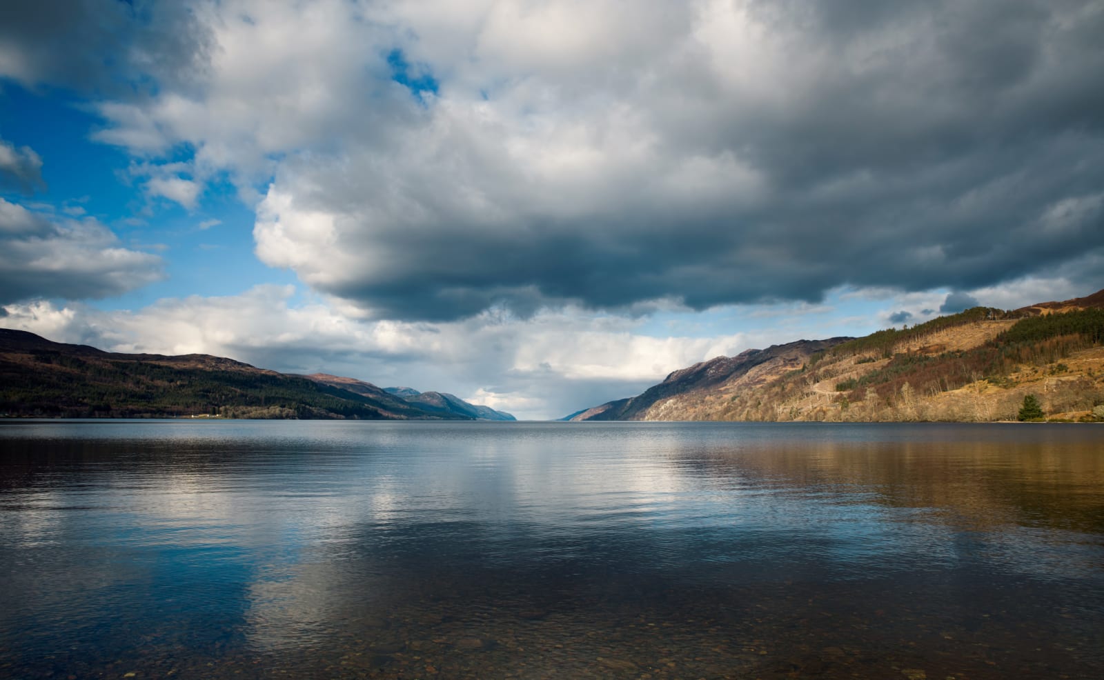 The calm and still waters of Loch Ness with rolling hills on either side