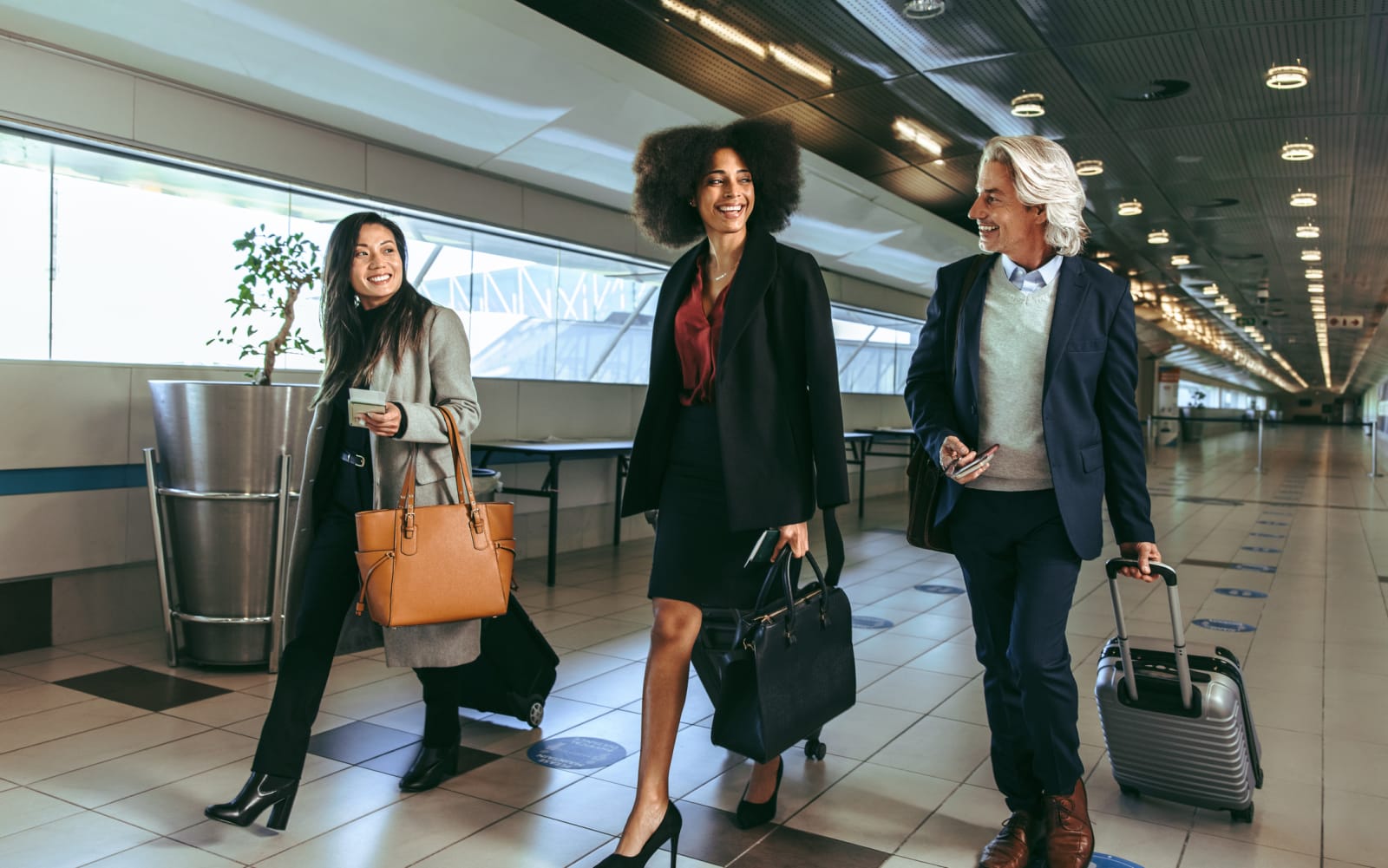 three business people with suitcases and handbangs walk through an airport 