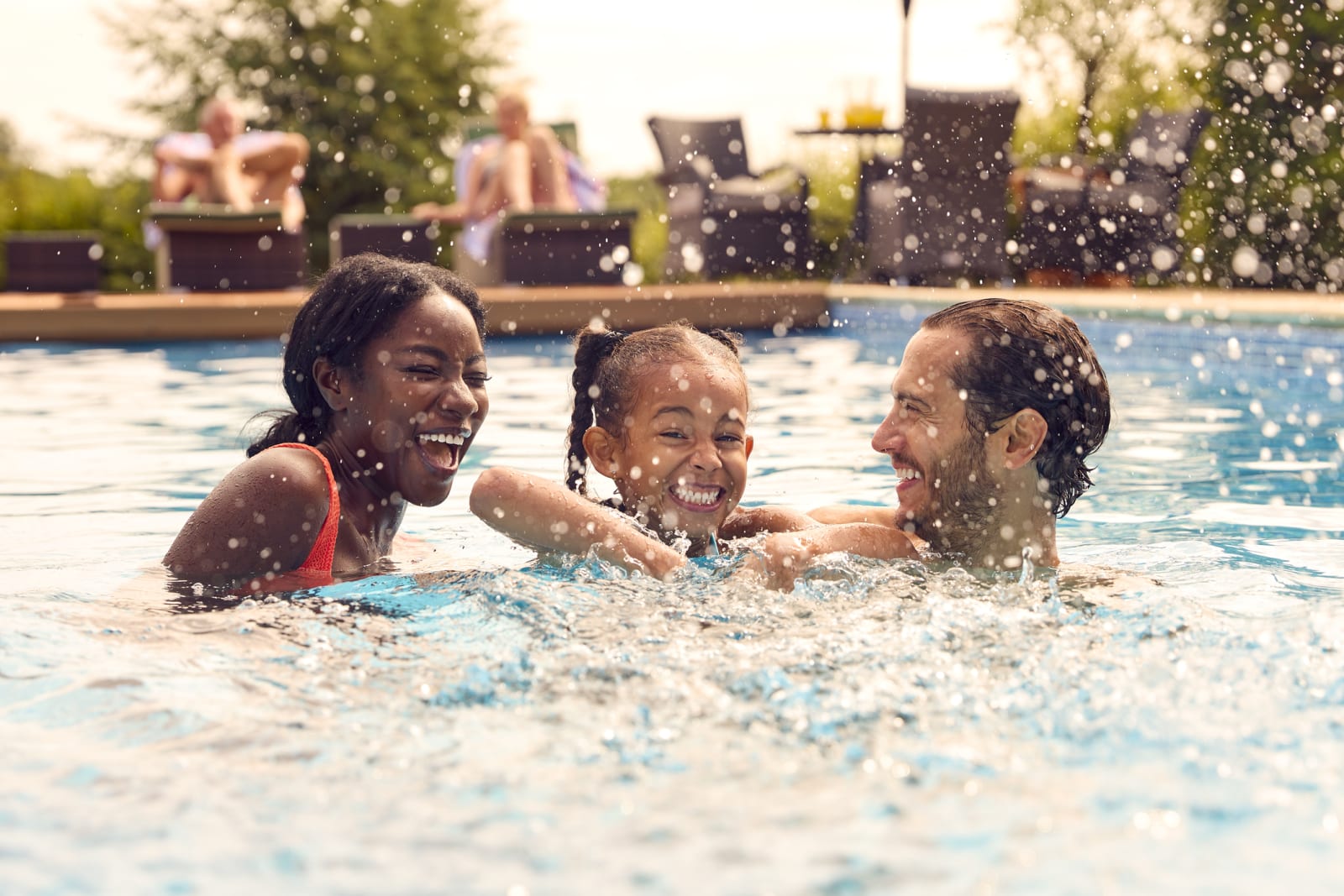 mother, father and daughter in pool splashing water