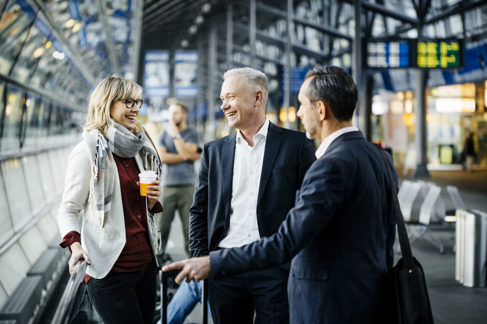 three people in business clothing stand talking in an airport