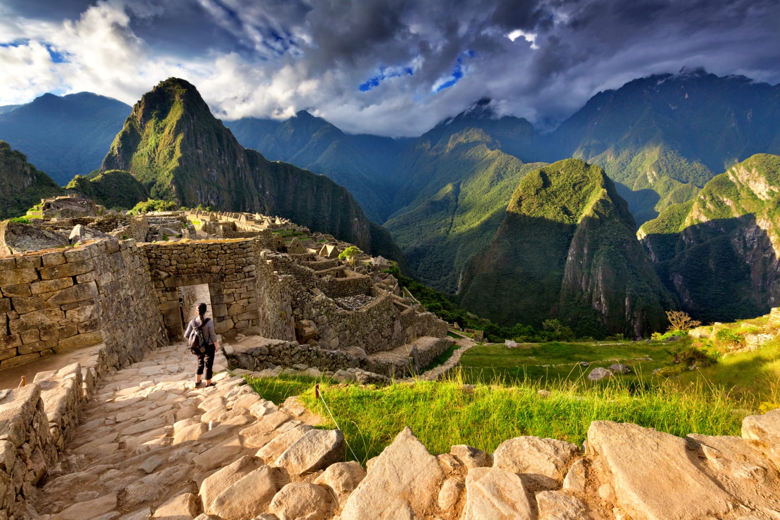 Back view of female tourist descending stairs overlooking Machu Picchu ruins at sunset, Peru