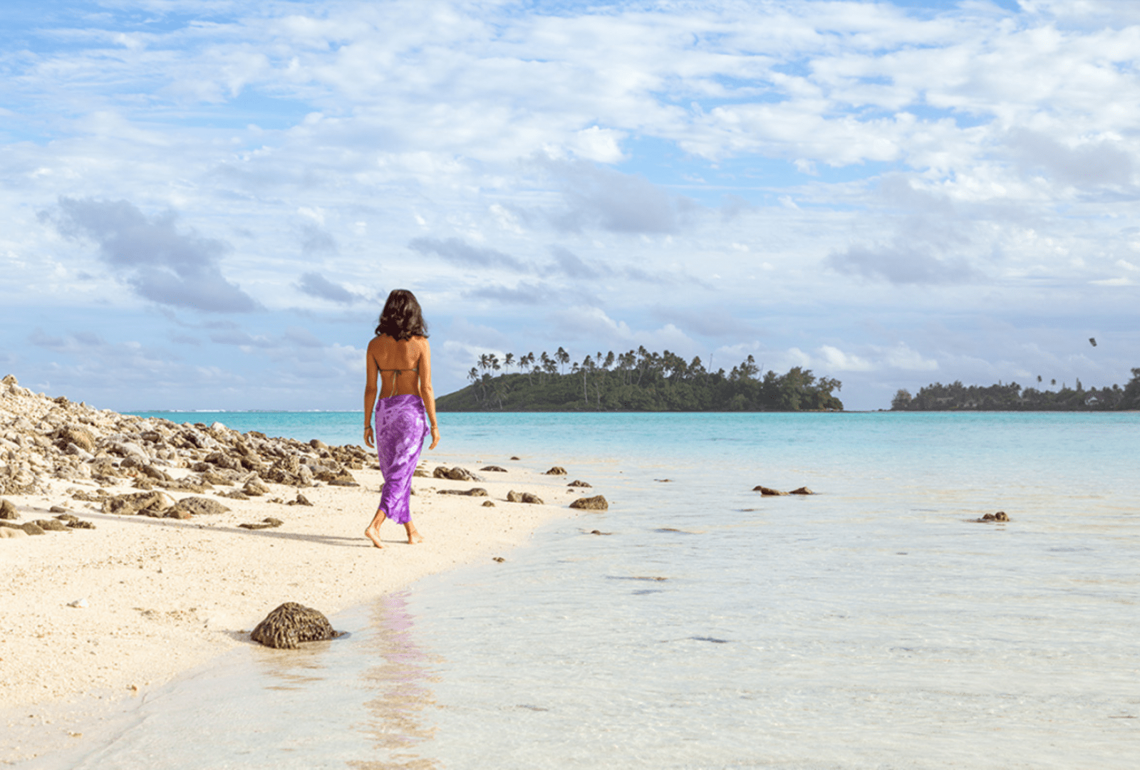 A woman walks across a beach in Rarotonga