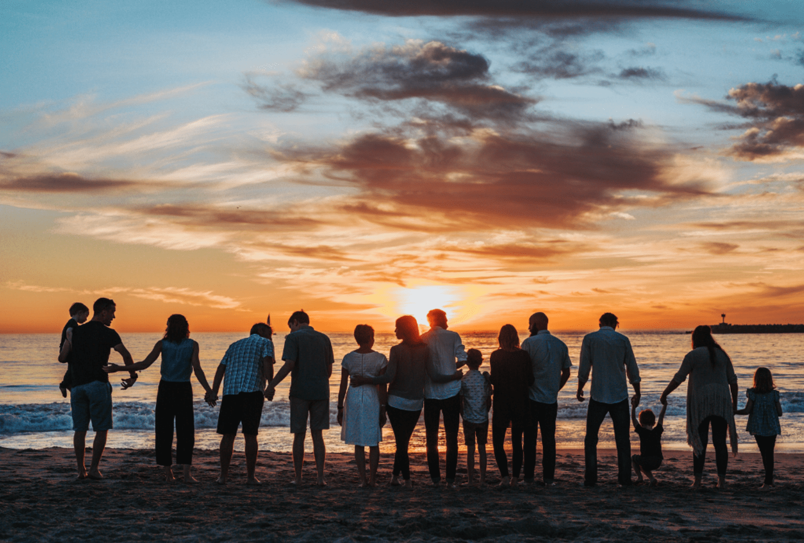 A large group of people gathers on a beach at sunset.